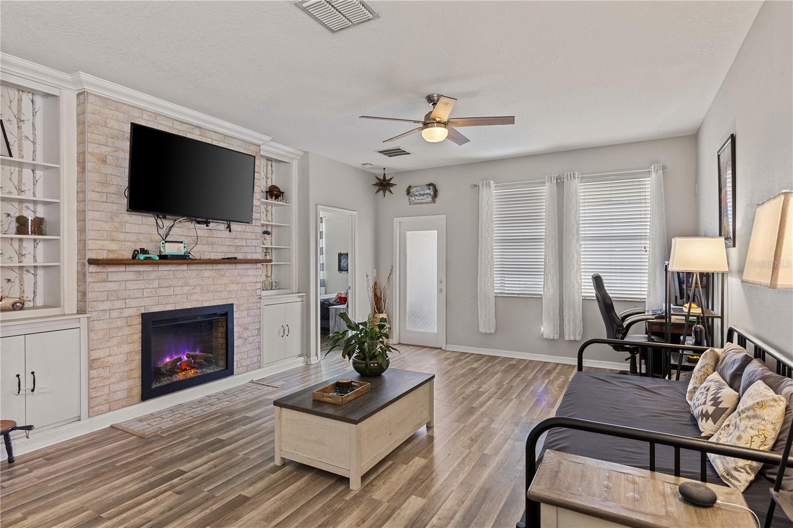 The living room boasts a white brick accent wall with an electric fireplace