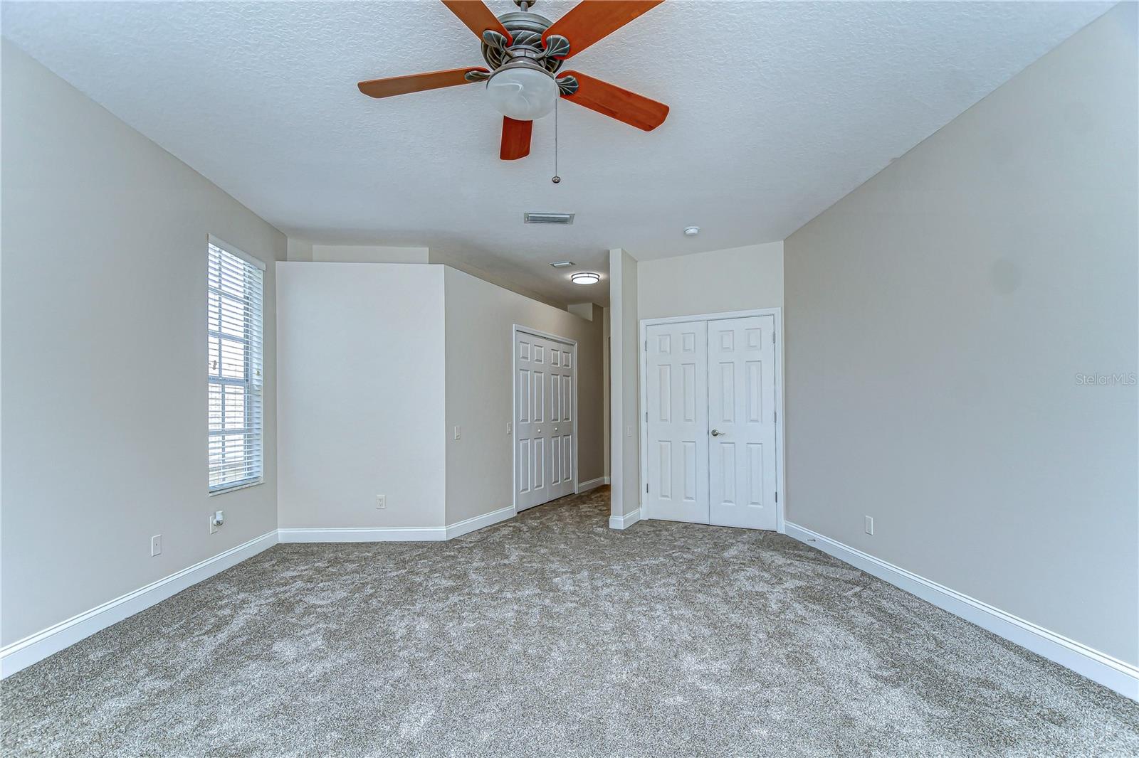 Experience tranquility in this spacious primary bedroom boasting plush carpeting, neutral tones, and a ceiling fan for comfort.