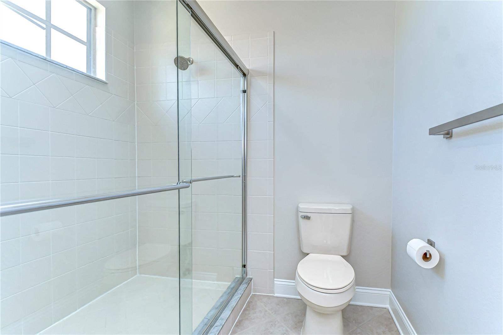 Step into modern comfort with this pristine bathroom, highlighting a sleek glass shower and fresh tilework