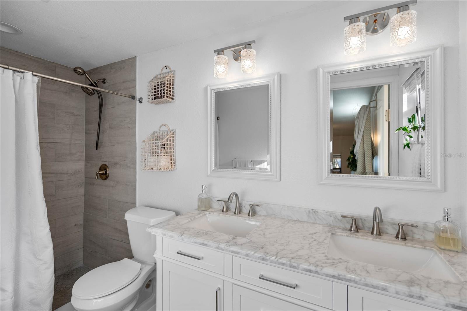 Tastefully remodeled primary en suite bathroom with large walk in shower, dual vanities, & updated lighting