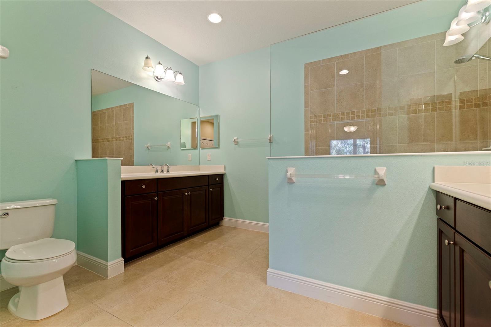 Primary ensuite bathroom with dual vanities, dual closets, and walk-in shower