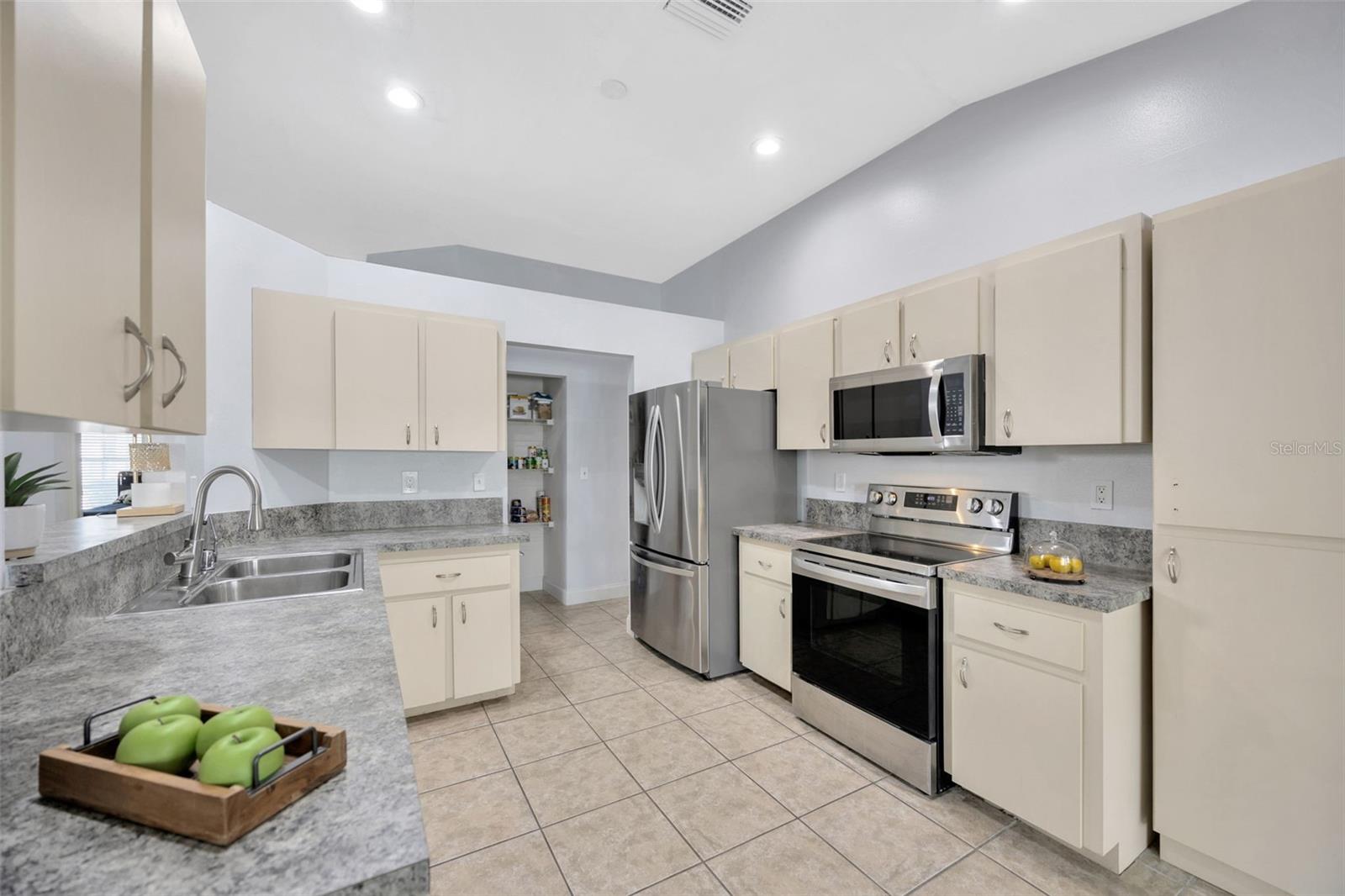 The dual-basin stainless steel sink is positioned under an open pass-through to the dining or living area, enhancing the flow and openness of the kitchen.