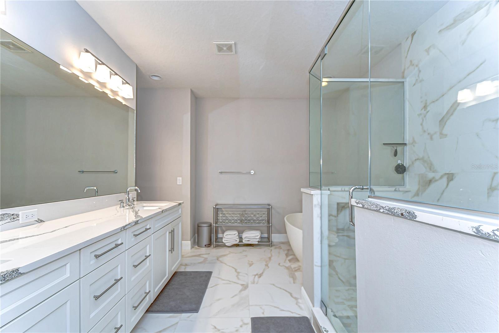 Indulge in spa-like serenity with this opulent bathroom featuring sleek dual vanities, a luxurious glass-enclosed shower, and elegant marble finishes, offering the perfect oasis for relaxation and rejuvenation.