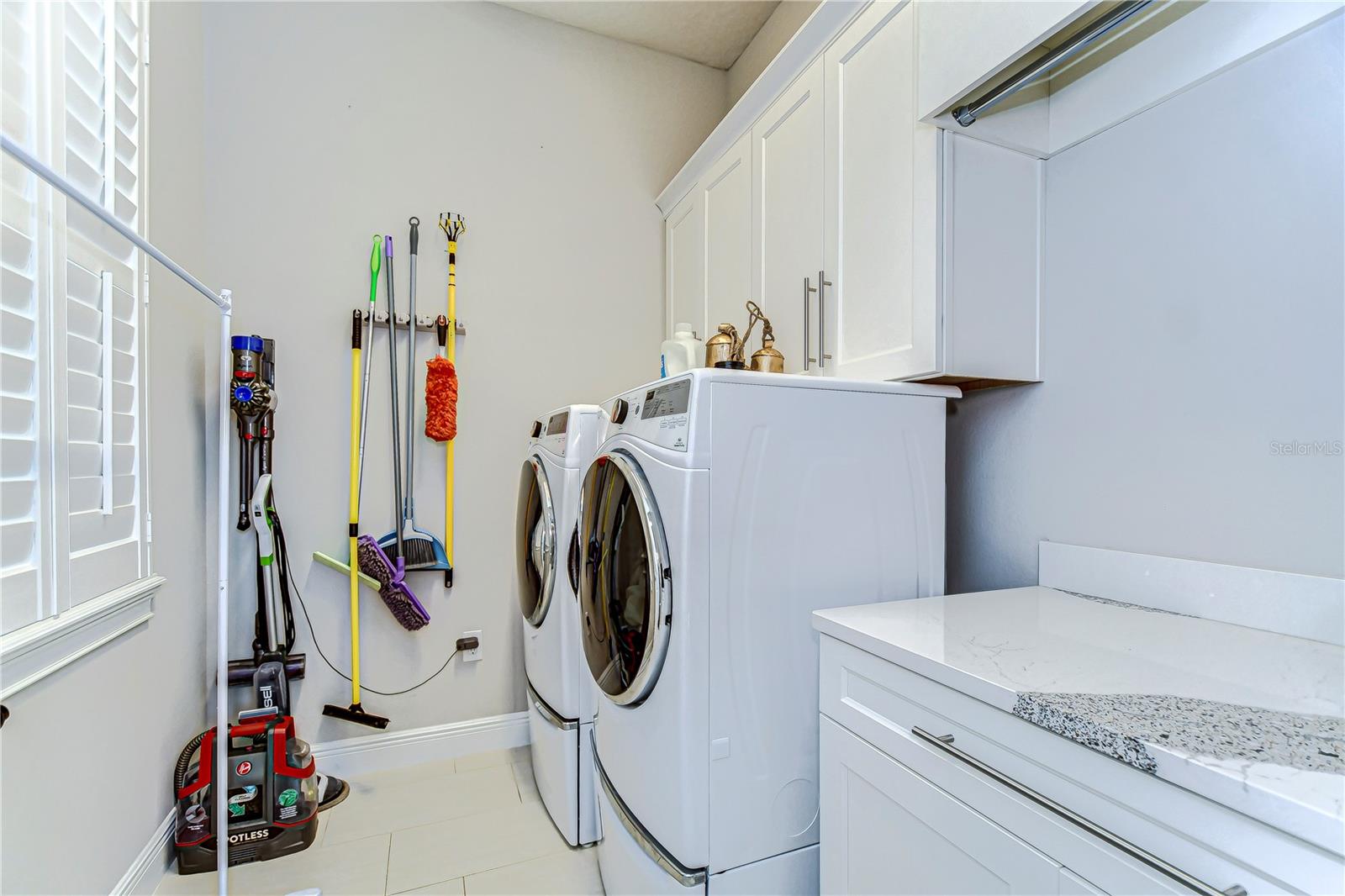 Effortlessly tackle laundry day in this chic and airy utility room, featuring sleek countertops and abundant cabinetry.