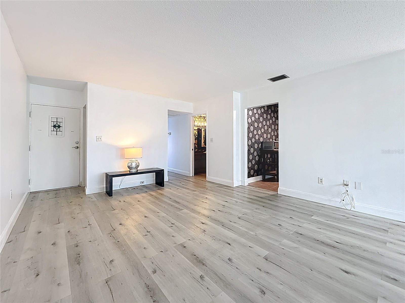 You are in the bonus sitting area/home office space, view towards the front door (left side) and the kitchen access, plus the hallway leading to the bedrooms & baths.