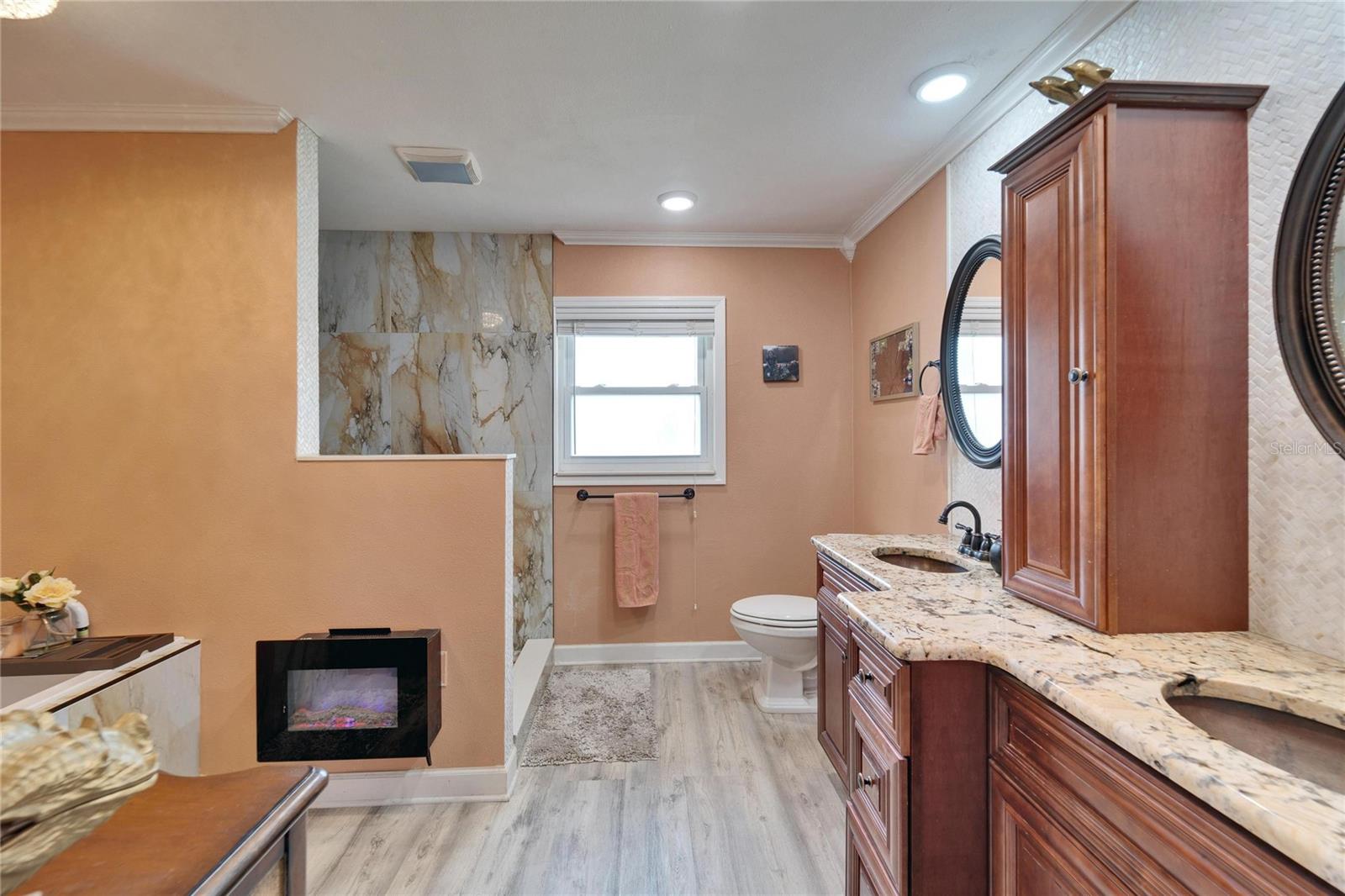 Primary bathroom has tall counter dual vanity with granite countertops and an electric fireplace