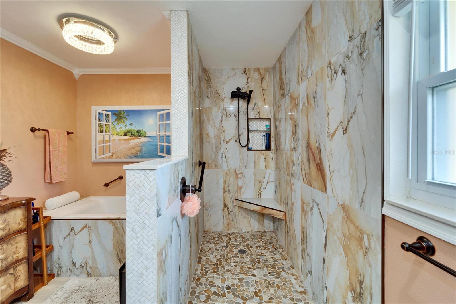 Large, tiled shower with a flat river rock floor has a grab bar and seat