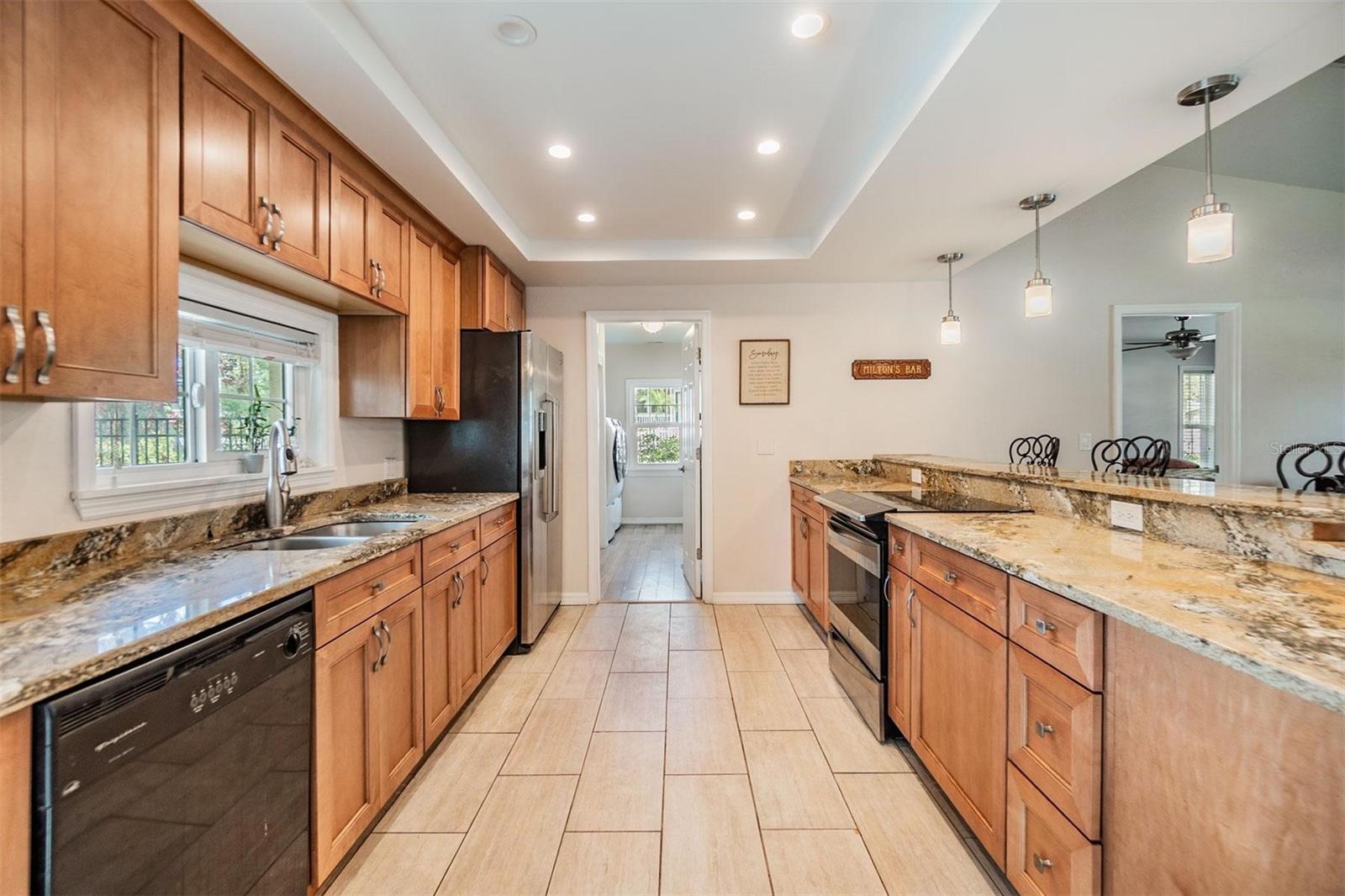 Beautifully updated kitchen with granite countertops, striking cherry wood cabinets, stainless steel stove and refrigerator, plank tile flooring, and elevated breakfast counter overlooking the living room.