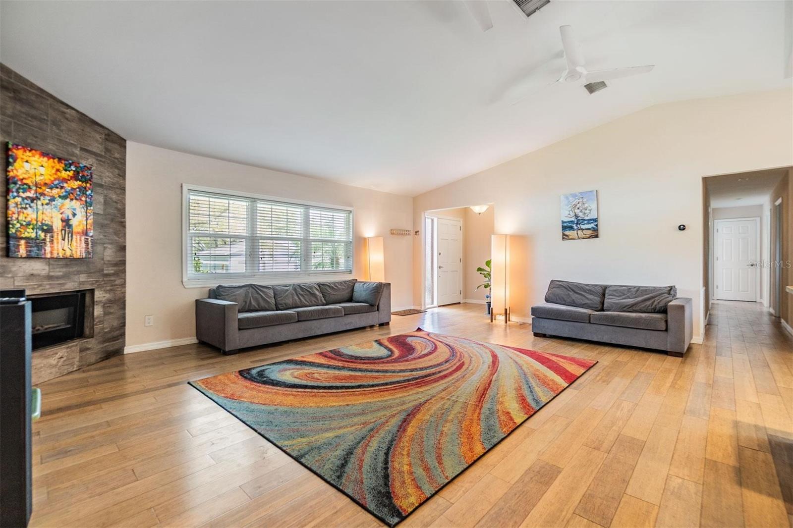 Beautifully updated open concept living space featuring vaulted ceilings, glass sliders to the back patio, a corner fireplace, and gorgeous wood floors.