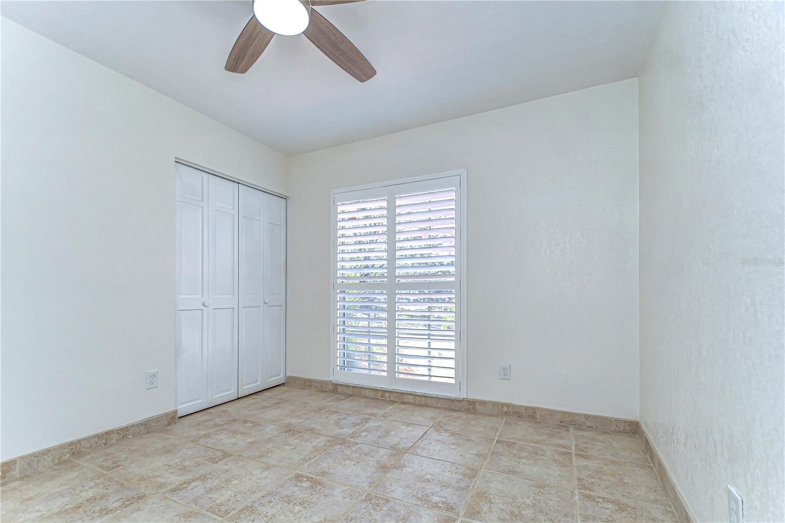 This bright and airy bedroom features elegant tile flooring and a ceiling fan, promising comfort and style.