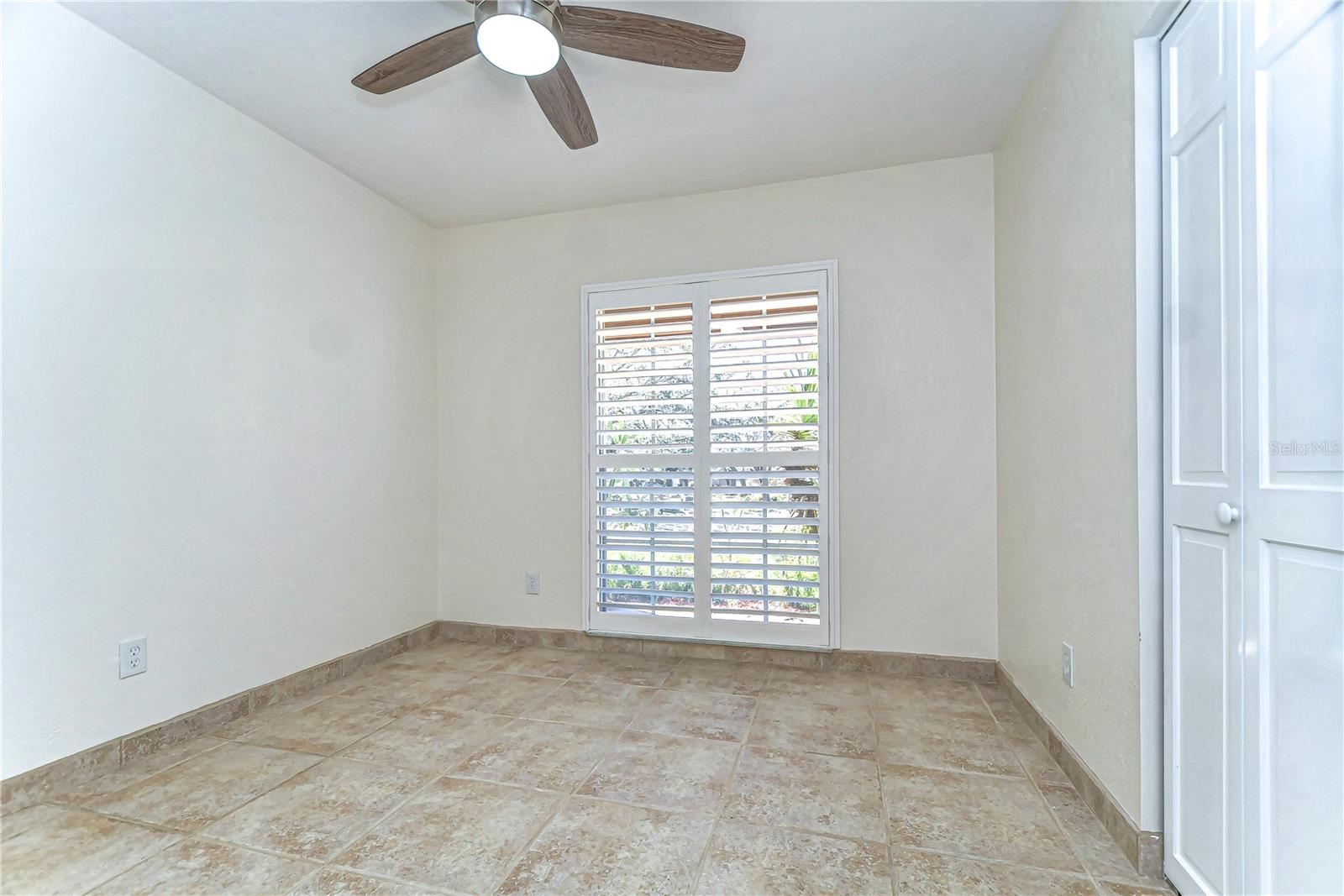 Step into a world of possibilities in this inviting bedroom, complete with elegant tile flooring and abundant natural light filtering through stylish plantation shutters.