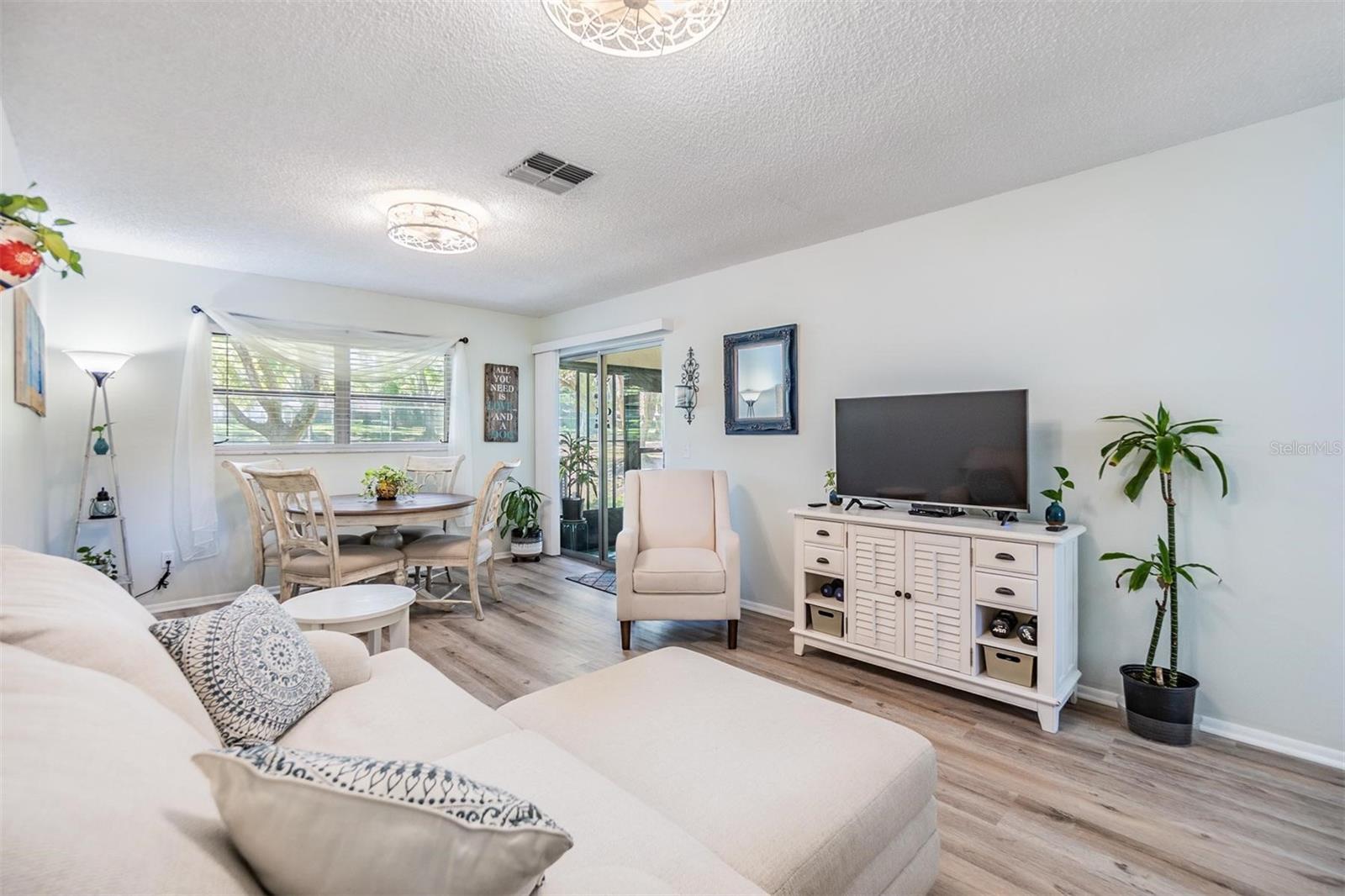 Light and bright living room and dining room with luxury vinyl plank flooring, pass through window to kitchen, and glass sliders out to the lanai.