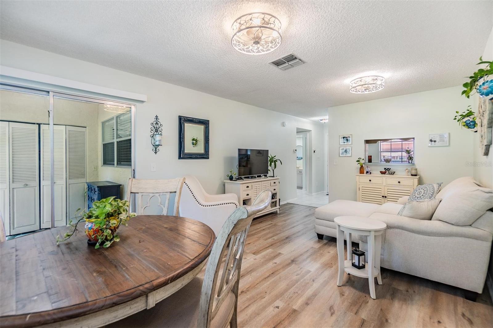 Light and bright living room and dining room with luxury vinyl plank flooring, pass through window to kitchen, and glass sliders out to the lanai.