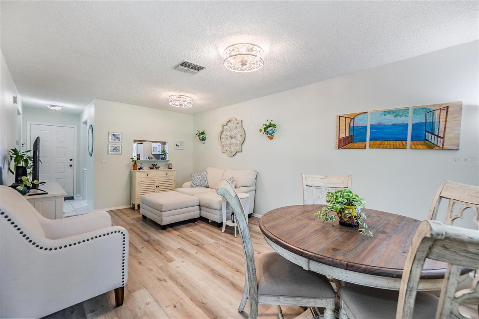 Light and bright living room and dining room with luxury vinyl plank flooring, pass through window to kitchen, and glass sliders out to the lanai.