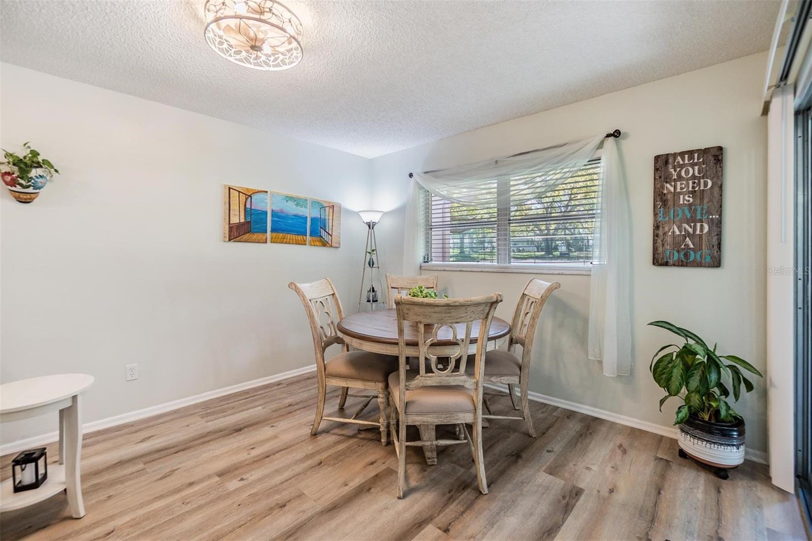 Light and bright living room and dining room with luxury vinyl plank flooring, pass through window to kitchen, and glass sliders out to the lanai.