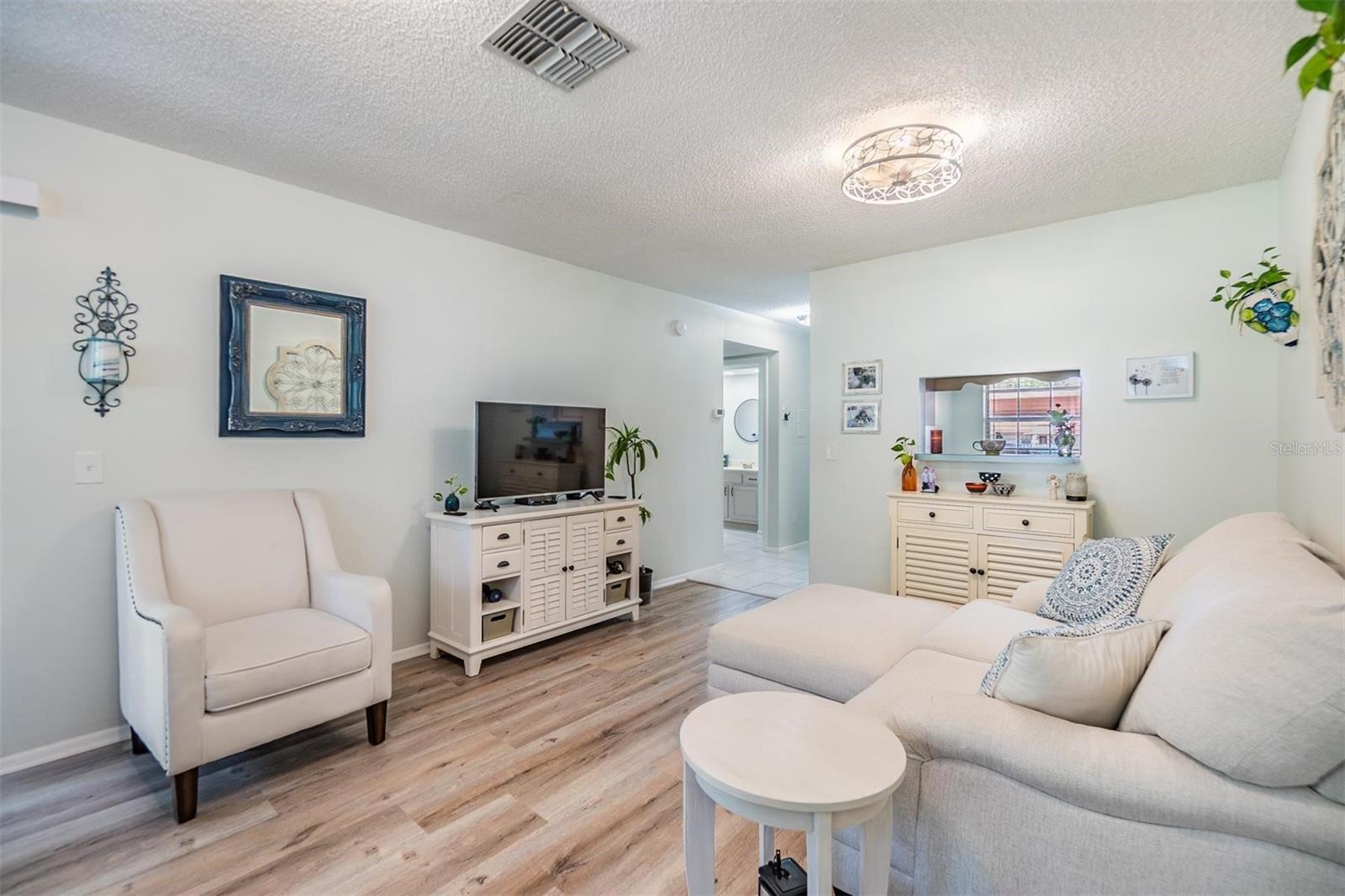 Light and bright living room and dining room with luxury vinyl plank flooring, pass through window to kitchen, and glass sliders out to the lanai.
