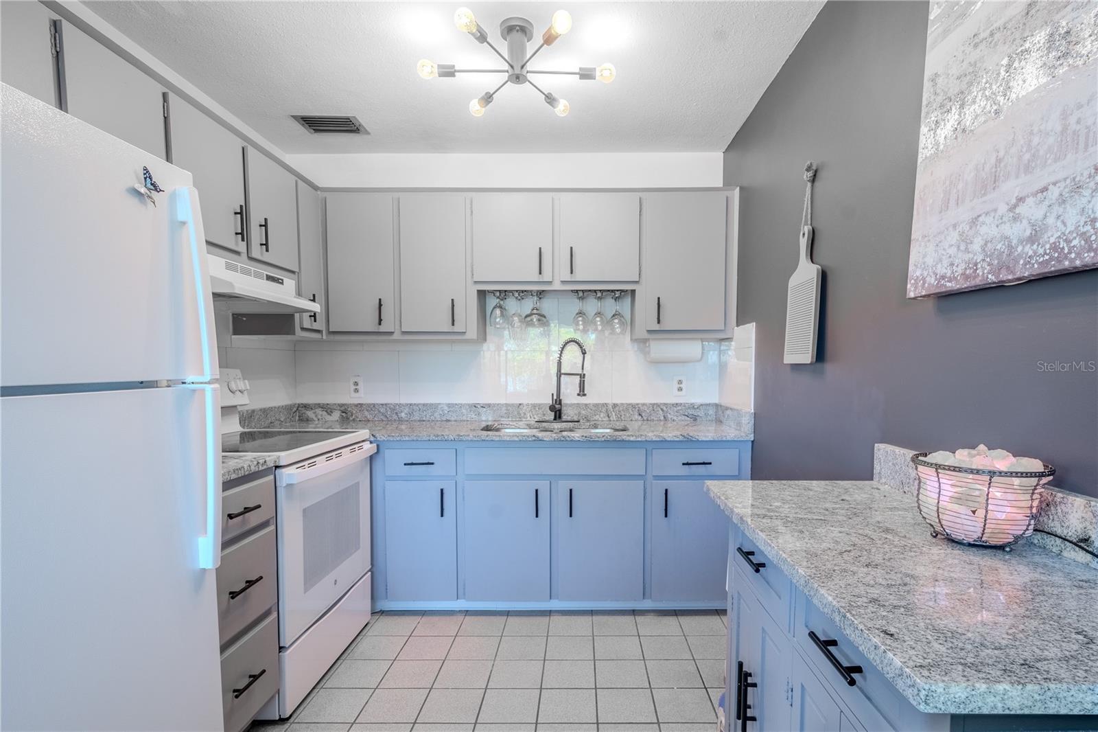 The kitchen features a modern light fixture, tile floor and granite countertops.