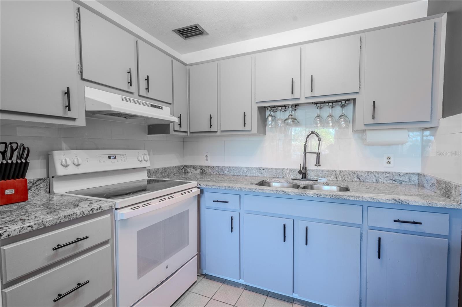 the kitchen features a deep, dual stainless sink sink with Faucet with Spray Head, an Under Cabinet Mount Stemware Rack and tile backsplash.