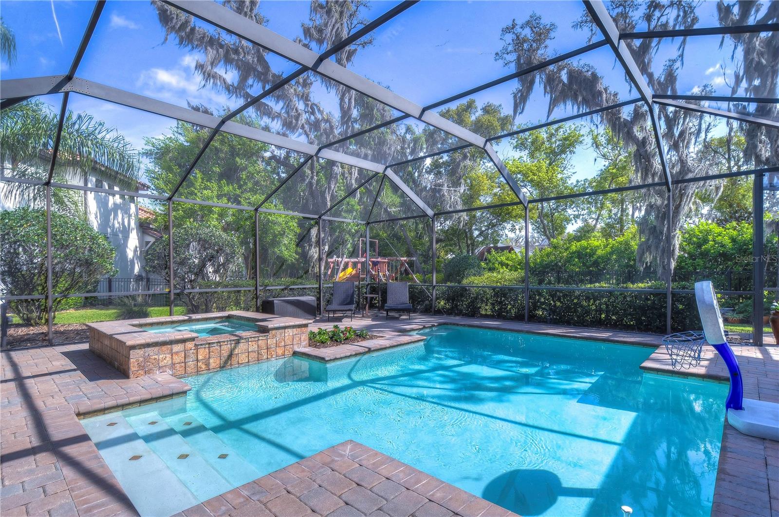 Dive into luxury with this exquisite screened-in pool and spa area, perfect for all-year entertainment against a backdrop of lush greenery.