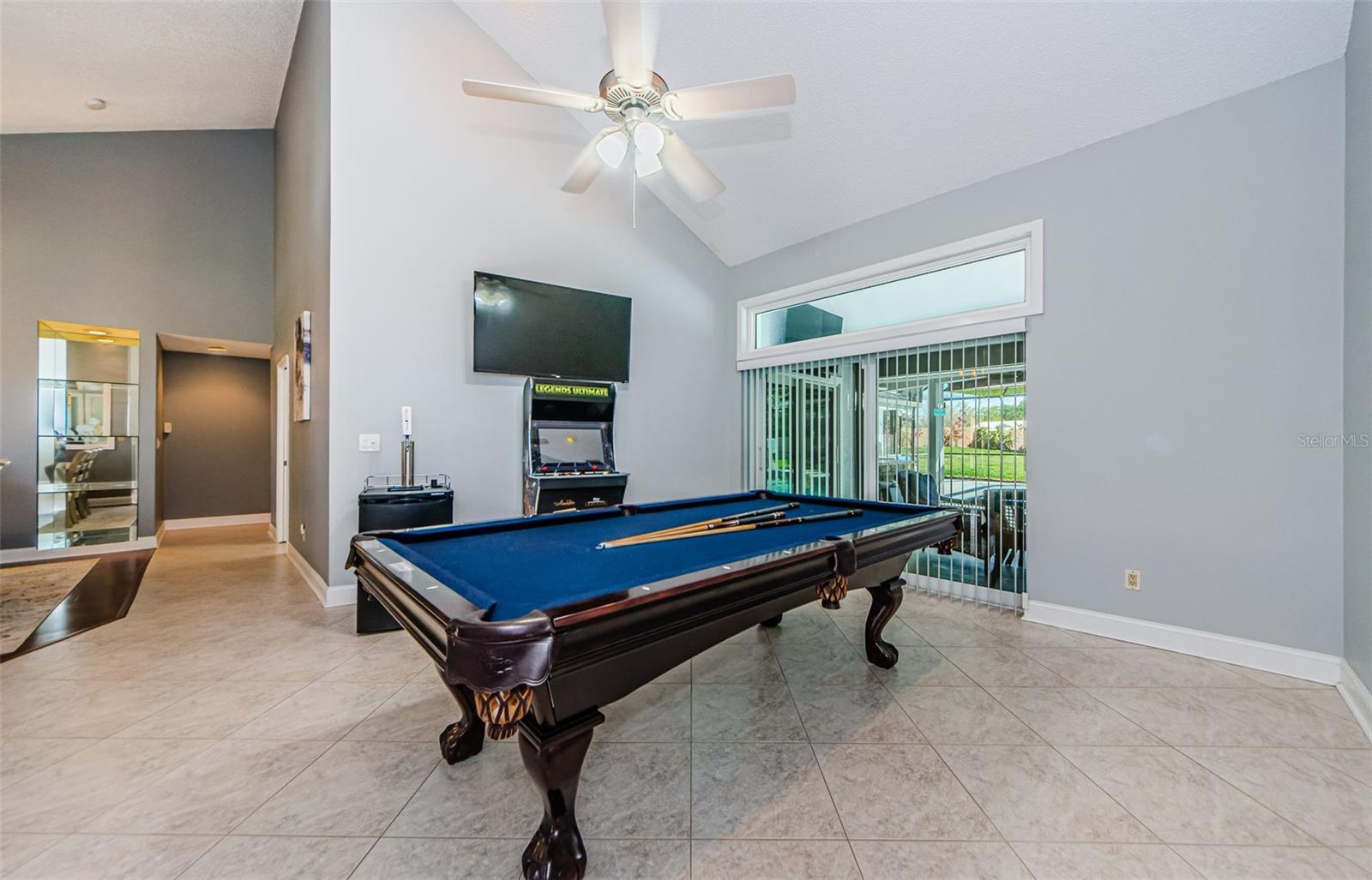 Large living room with Cathedral  ceilings used as an entertainment room housing pool table, TV and new glass sliding doors out to the pool area.