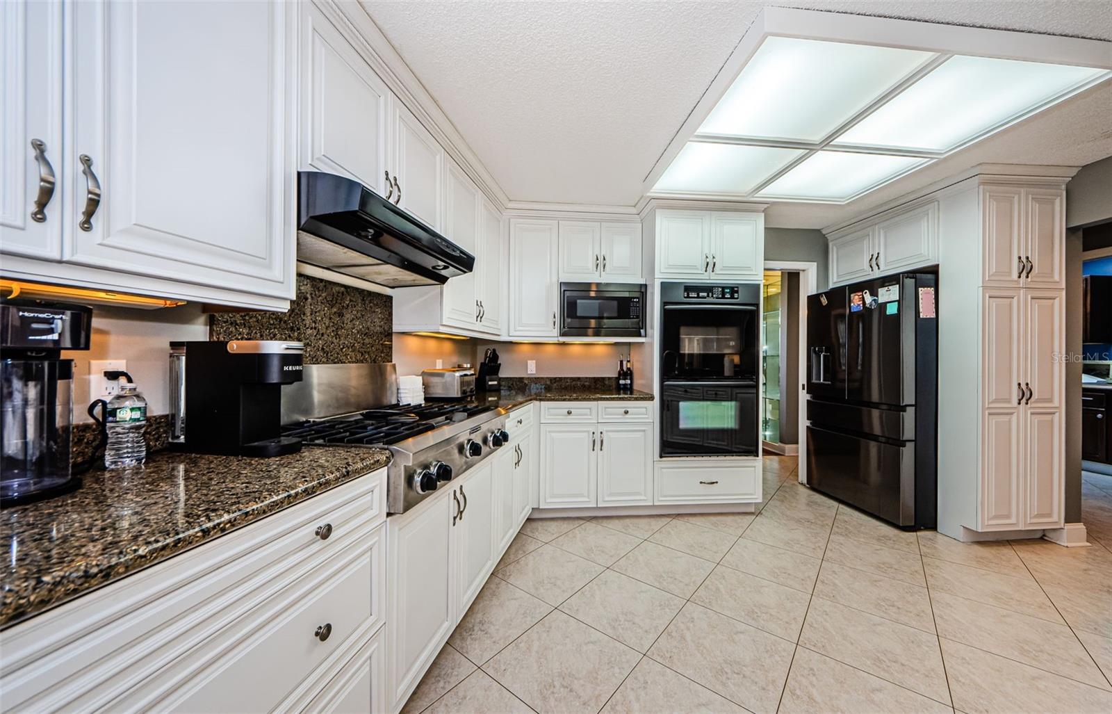 Here is same side of kitchen showing granite counter, gas stove top, exhaust system, microwave, double oven with one convection, and newer refrigerator.