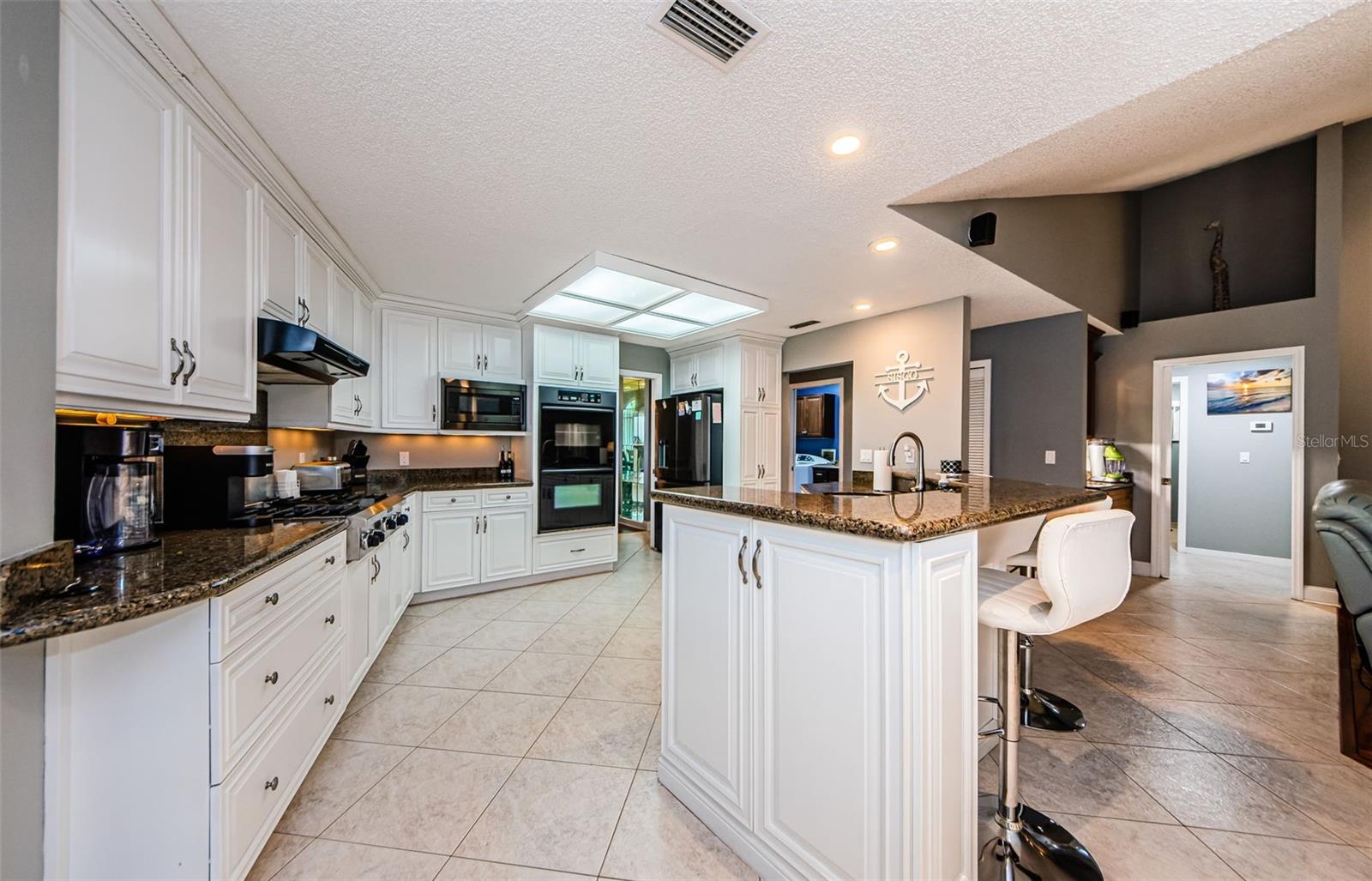 Big open view of this stunning kitchen with under counter lighting, overhead cam lighting, breakfast bar, all leading to buffet counter unit, just behind breakfast bar.