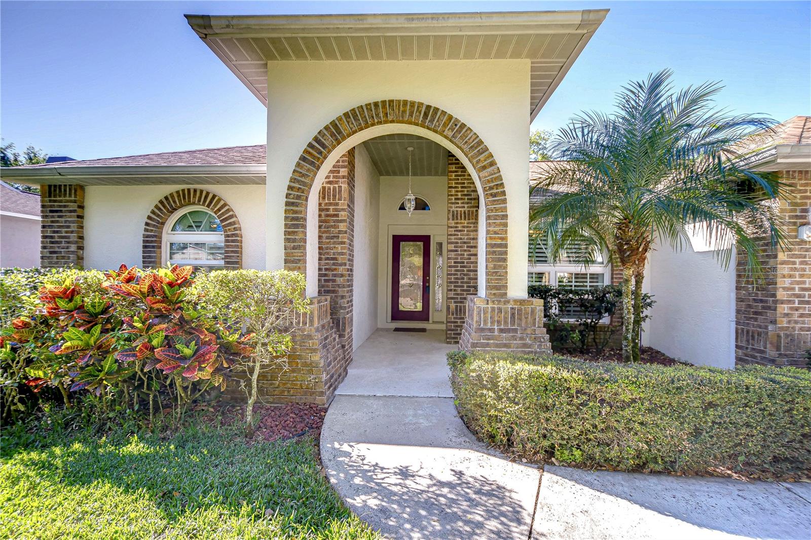 Step into a warm welcome with this stunning home, where a charming brick archway leads you through a lush garden entry.