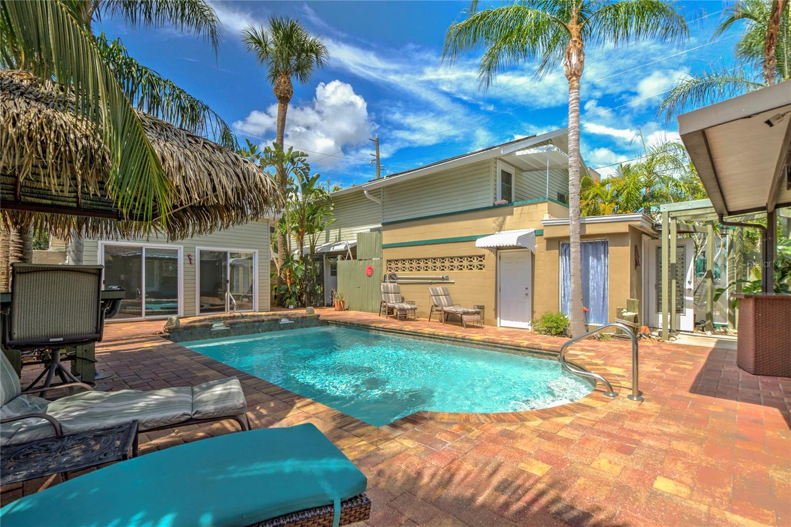 back yard with tiki hut and outdoor bath in blue behind palm tree