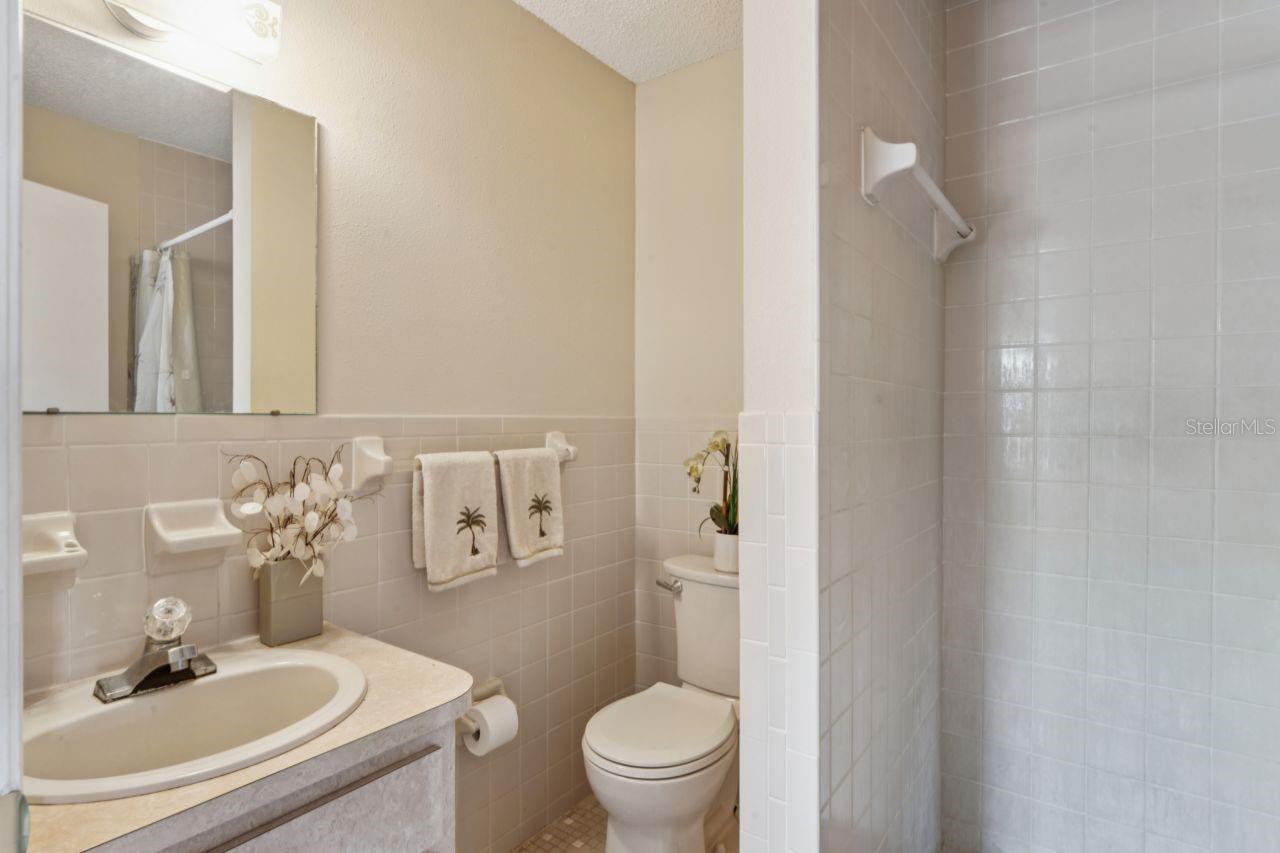 The primary bathroom features a single vanity, a walk-in shower without a tub, ceramic tile flooring, and a large mirror.