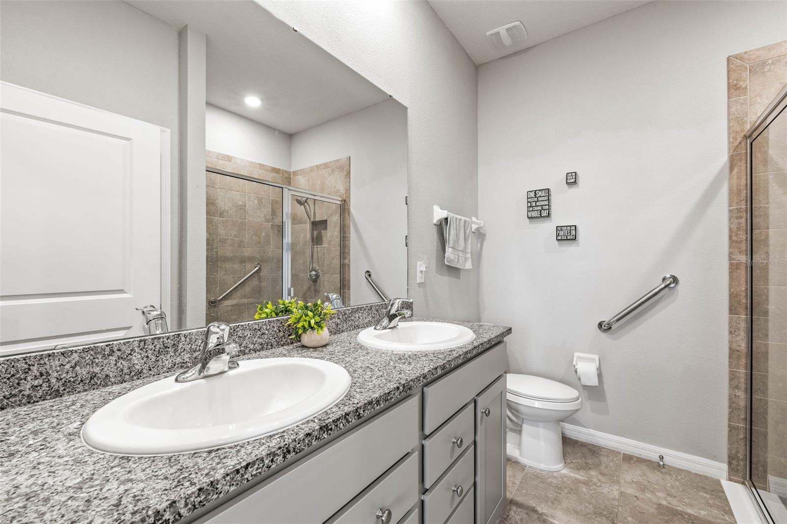 The primary bath has 2 sinks, shower entry, and bright lighting.