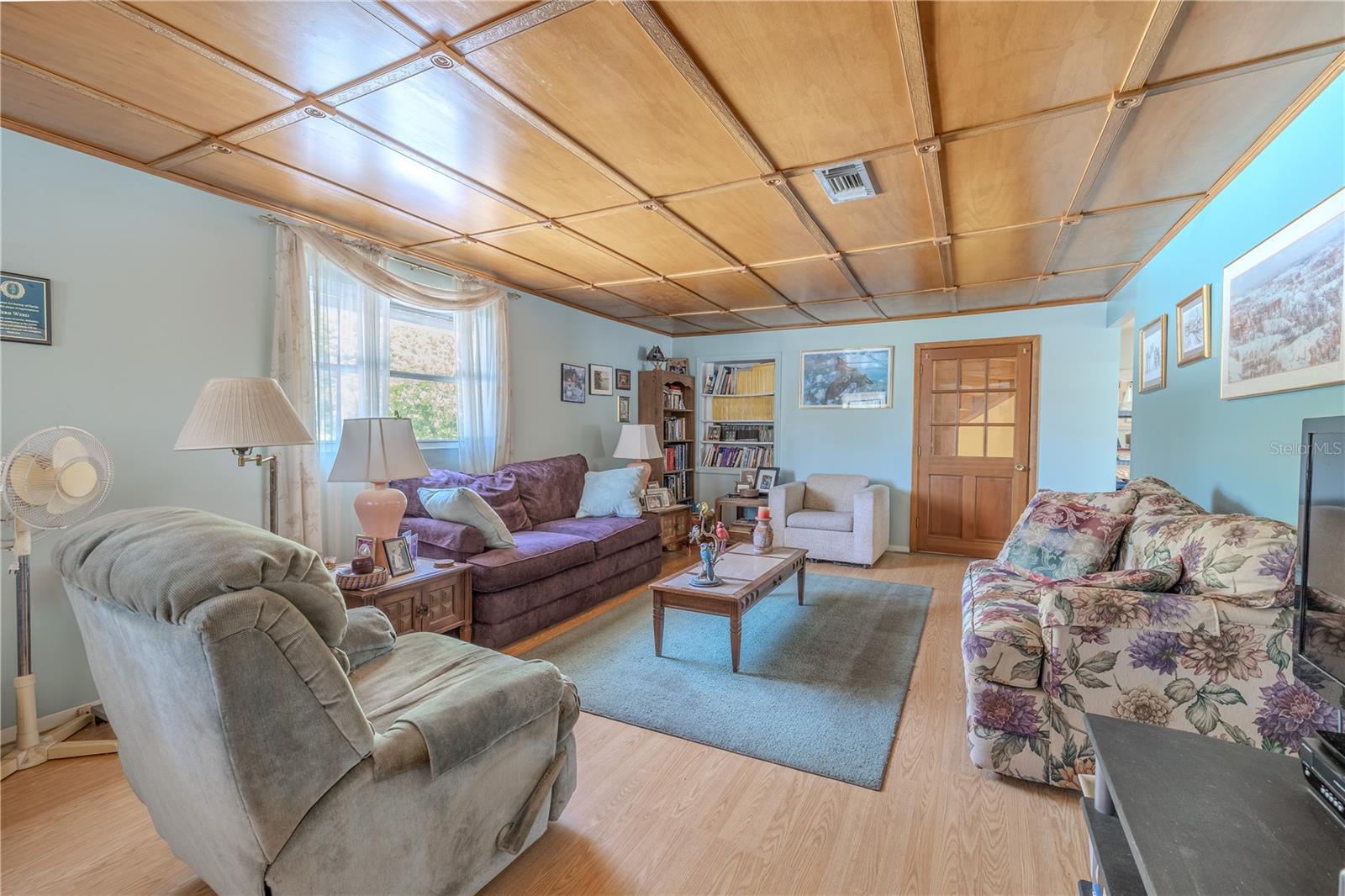 The living room features a decorative panel ceiling and wood look laminate floor.