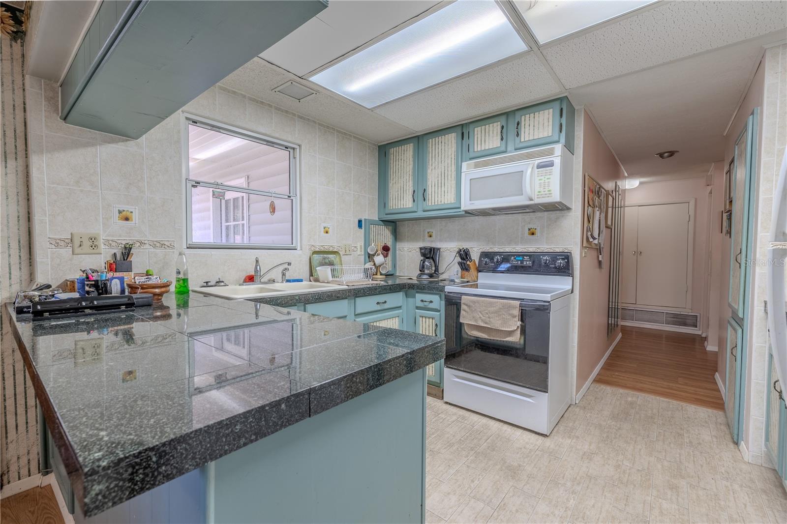 The kitchen features a tile floor, solid surface counters and a double basin kitchen sink beneath a window.