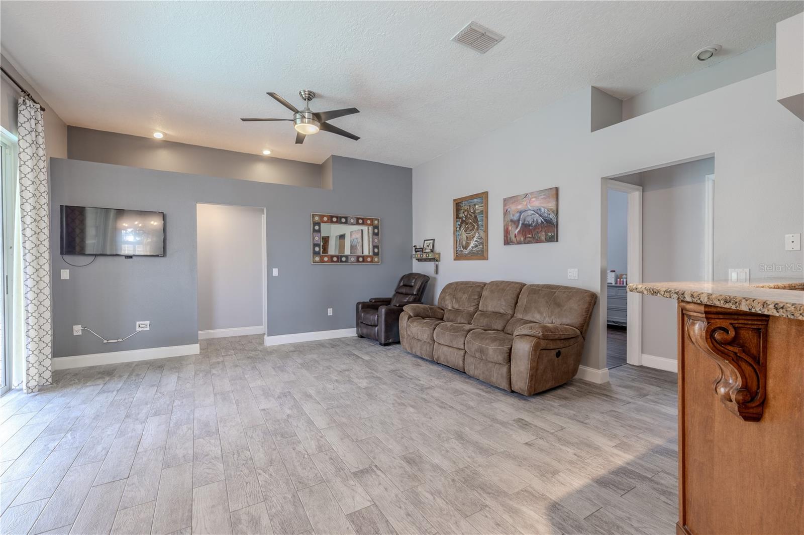 The family room features wood look plank tile flooring, recessed lighting and a modern ceiling fan with light kit.