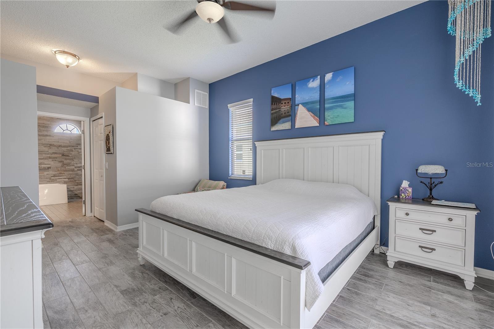 The primary bedroom features wood-look plank style tile flooring, a modern ceiling fan with light kit and an ensuite bath.