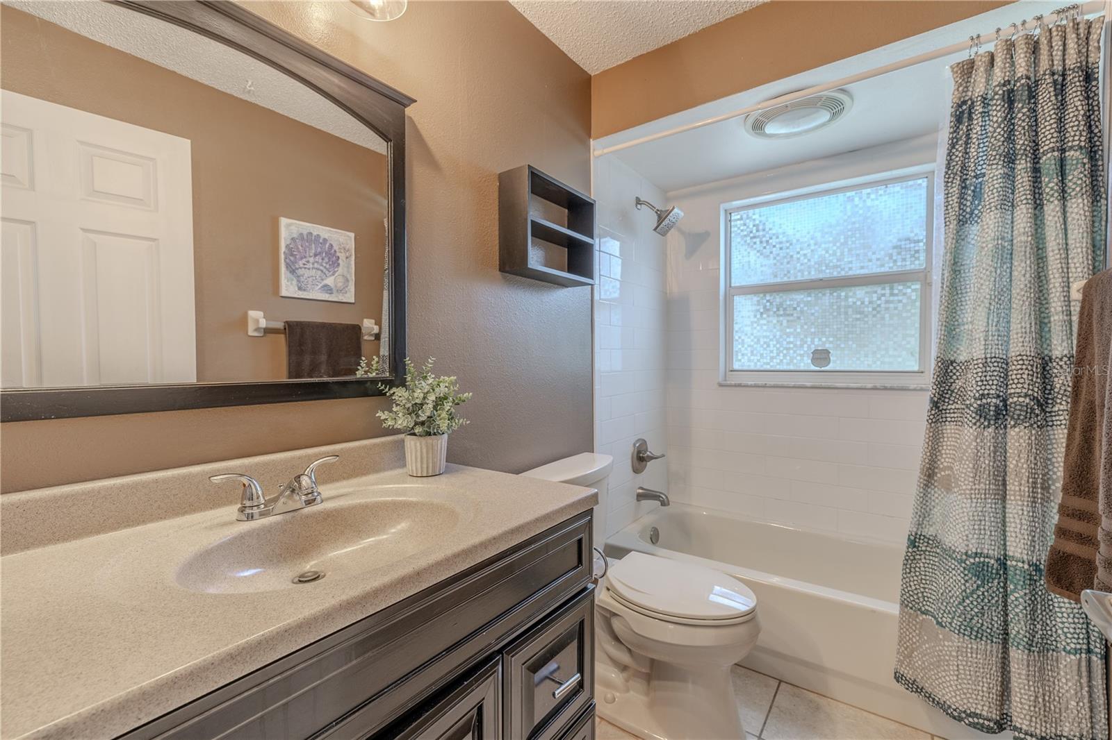 Bathroom 2 blends style and functionality with its updated vanity featuring rich wood cabinetry and a neutral countertop. The shower/tub combination with privacy window provides both convenience and natural light. Modern fixtures and thoughtful storage solutions complete this well-appointed space.