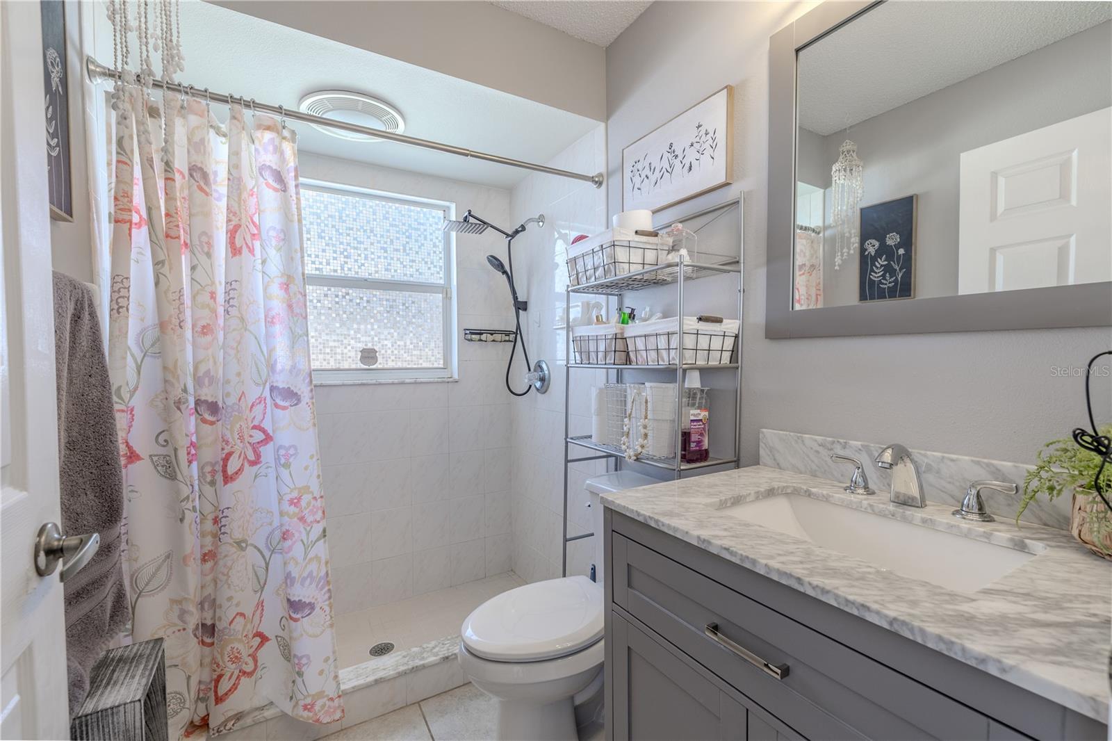 The third full bathroom offers both elegance and convenience with its direct pool access. Featuring a spacious walk-in shower, luxurious marble-look countertops, and contemporary gray cabinetry, this bathroom brilliantly balances style and practicality. Smart storage solutions and designer touches and a decorative light fixture create a sophisticated space that serves both everyday needs and poolside convenience.