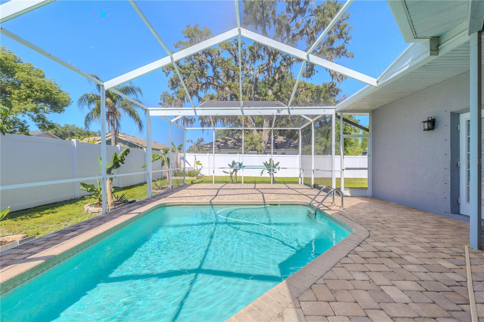 Experience the ultimate Florida lifestyle with this immaculate screened pool oasis. The spacious paver deck surrounds a pristine pool, all protected by a high-quality screen enclosure that allows for bug-free enjoyment while maximizing natural light. Privacy fencing and tropical landscaping create a serene retreat atmosphere, while direct home access and convenient features ensure effortless entertaining. Enjoy year-round swimming in this perfectly maintained outdoor sanctuary.