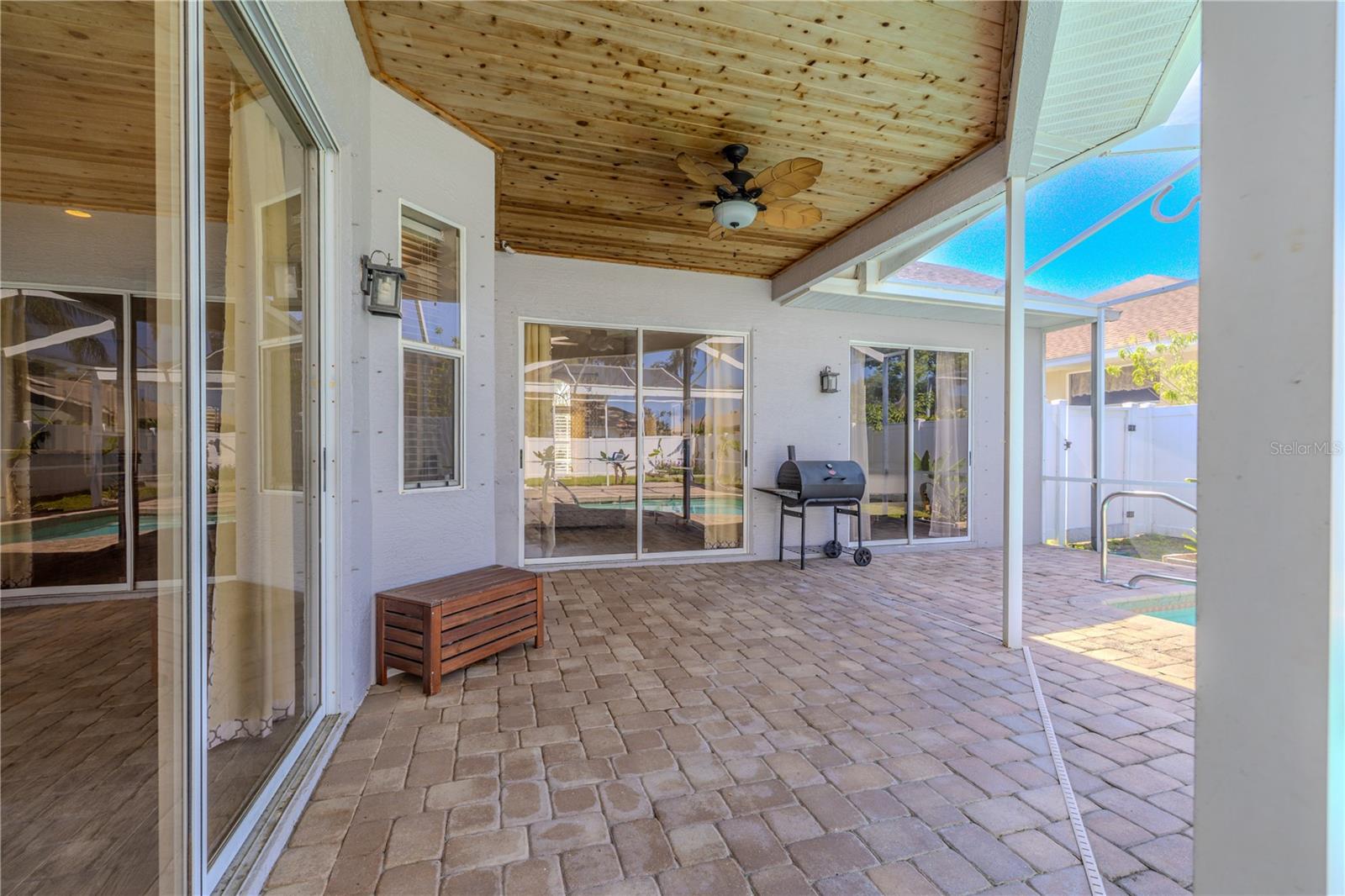 Entertain in style under the covered patio, where thoughtful design meets outdoor comfort. The tceiling with tropical fan creates a resort-like atmosphere, while multiple sliding glass doors provide seamless indoor-outdoor flow. Premium features include built-in lighting, paver stone flooring, and convenient grilling space – all while enjoying views of the sparkling pool. This sheltered retreat offers the perfect balance of protection and openness for year-round Florida living.