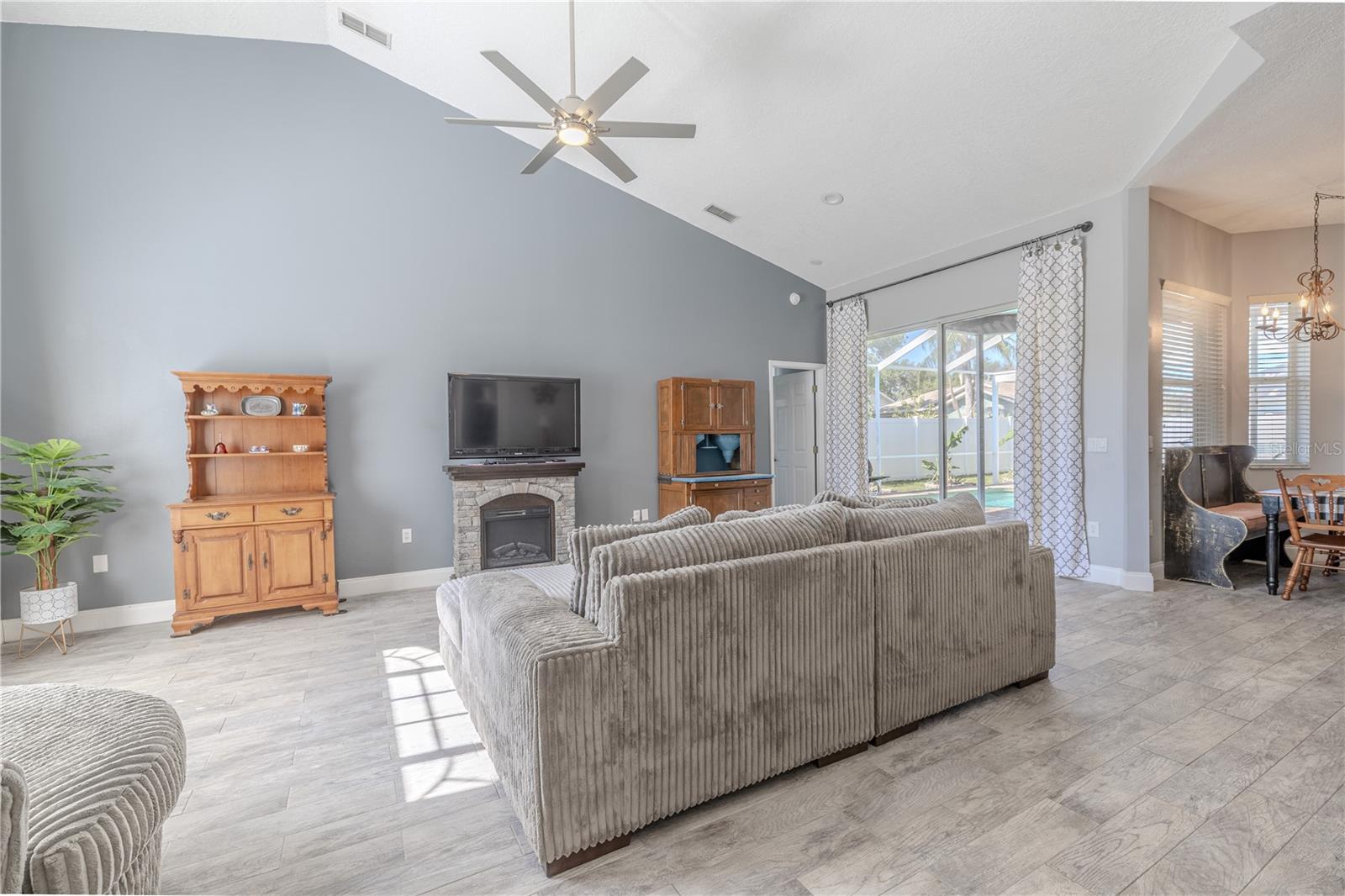 The living room features a vaulted ceiling with modern ceiling fan, neutral tone walls and wood-look tile floors