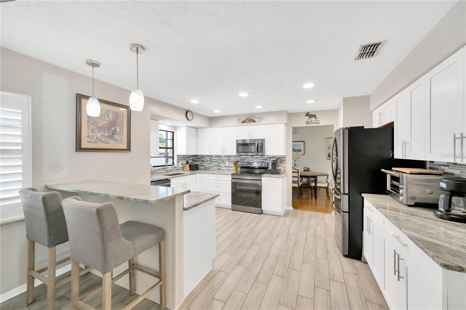 The adjacent kitchen is a chef’s and a baker’s dream, featuring black stainless steel appliances, plenty of stylish granite countertops, a sea glass backsplash, and a functional breakfast bar that opens to a casual dining area and the family room.