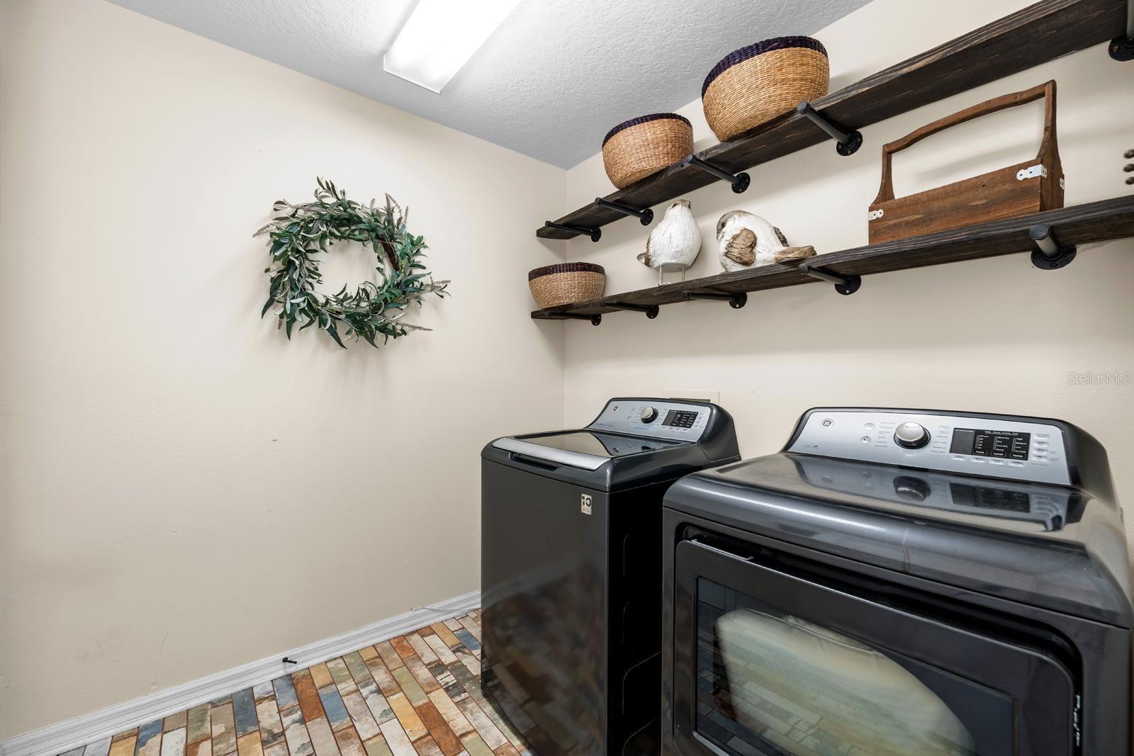 A spacious, inside laundry room with stylish open shelving and brick flooring!