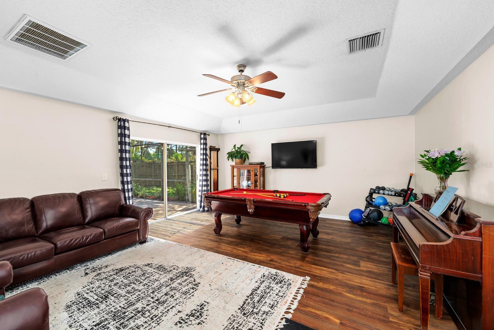 The huge bonus room features vinyl plank flooring, a tray ceiling, a lighted ceiling fan, and an oversized slider to the lanai and pool!  The pool table and equipment will stay with the home.
