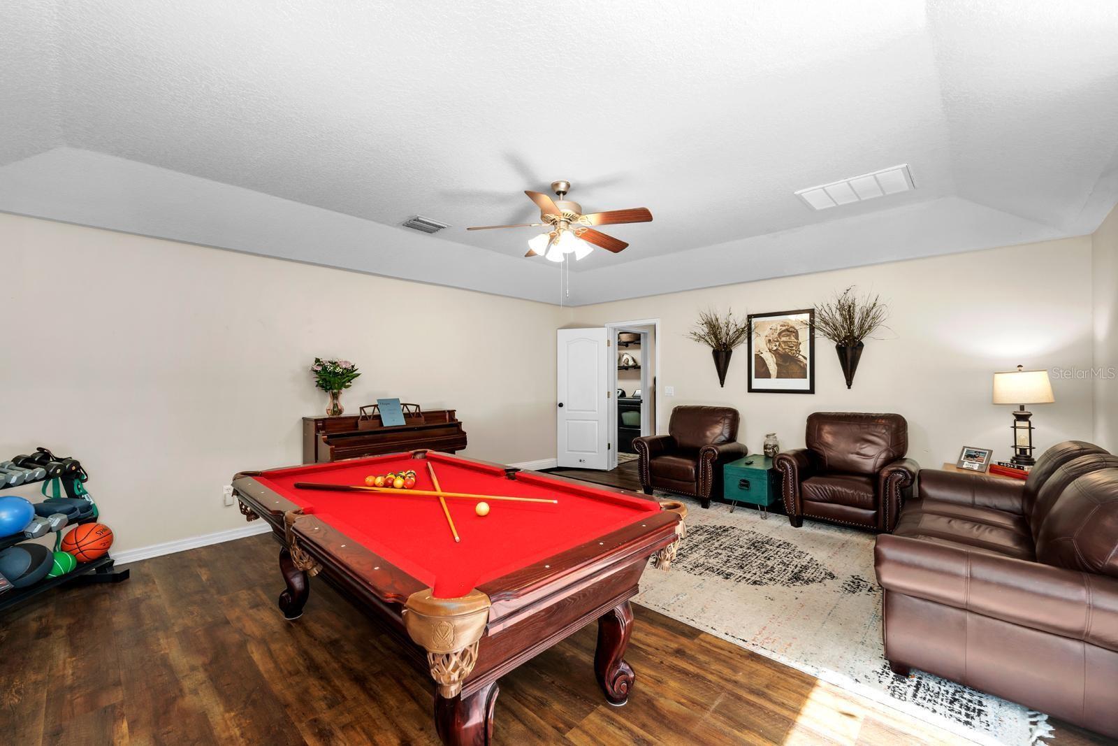 The huge bonus room features vinyl plank flooring, a tray ceiling, a lighted ceiling fan, and an oversized slider to the lanai and pool!  The pool table and equipment will stay with the home.