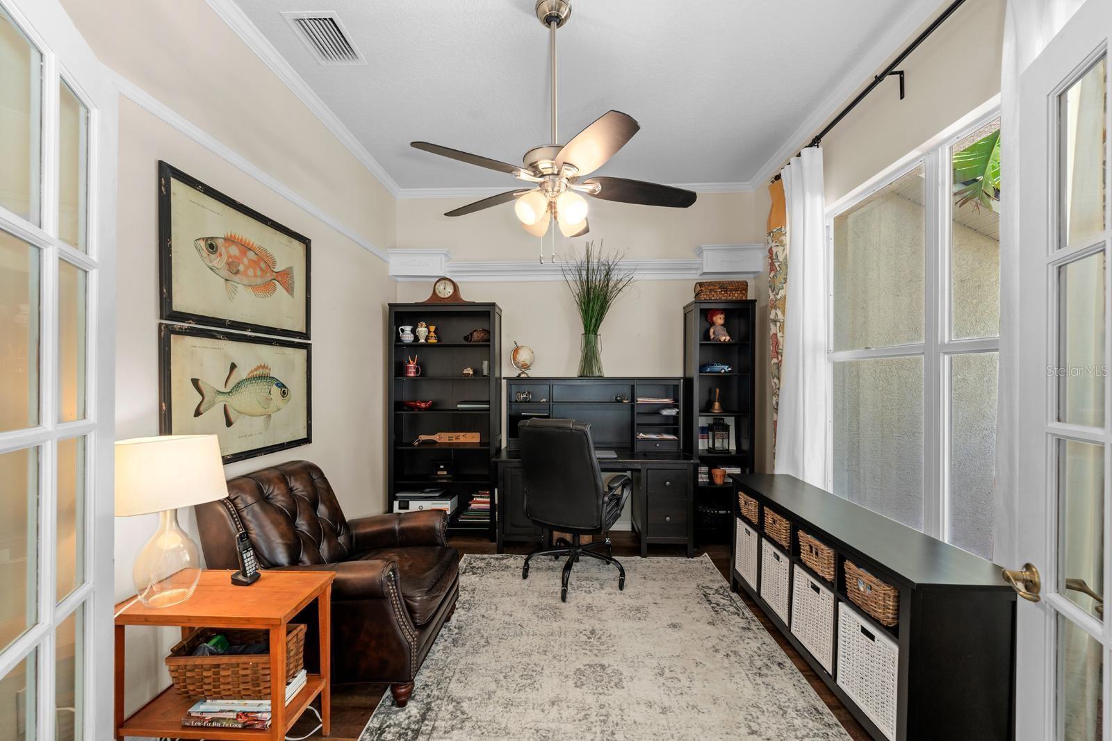Office/Den with crown molding, vinyl plank floors, french doors and a lighted ceiling fan.