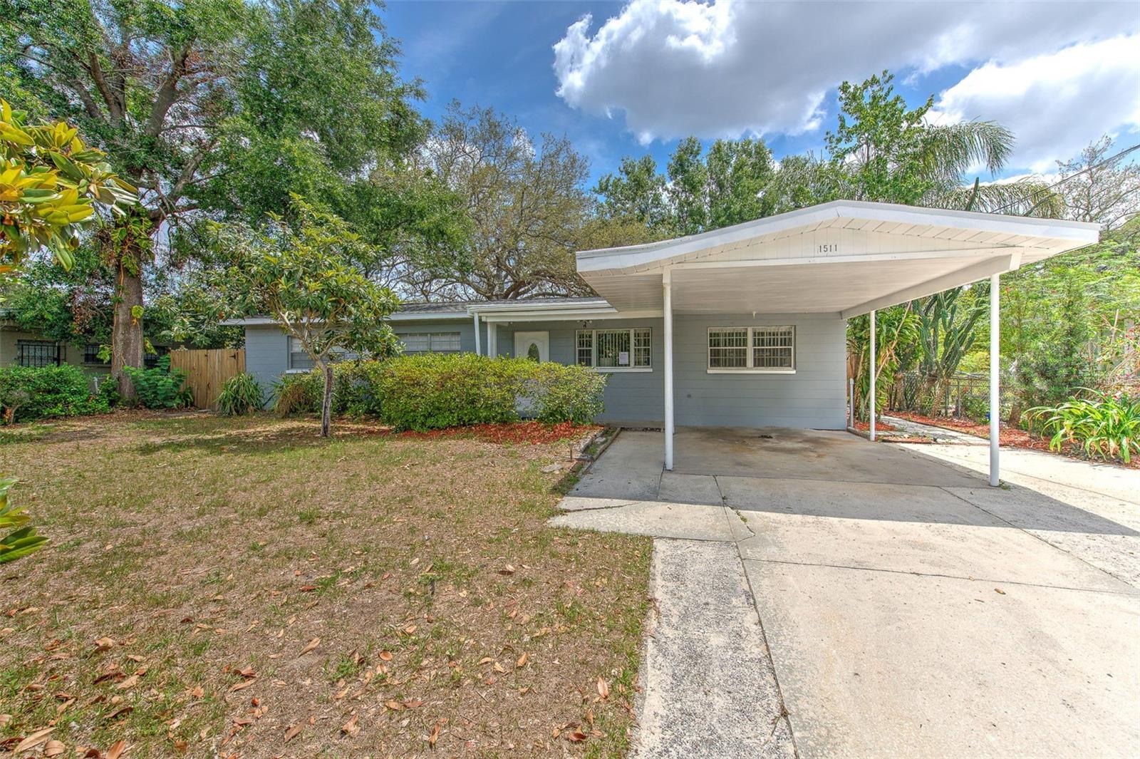 front of house with Loquat fruit tree and flowering magnolia tree. Wide driveway with a carport.