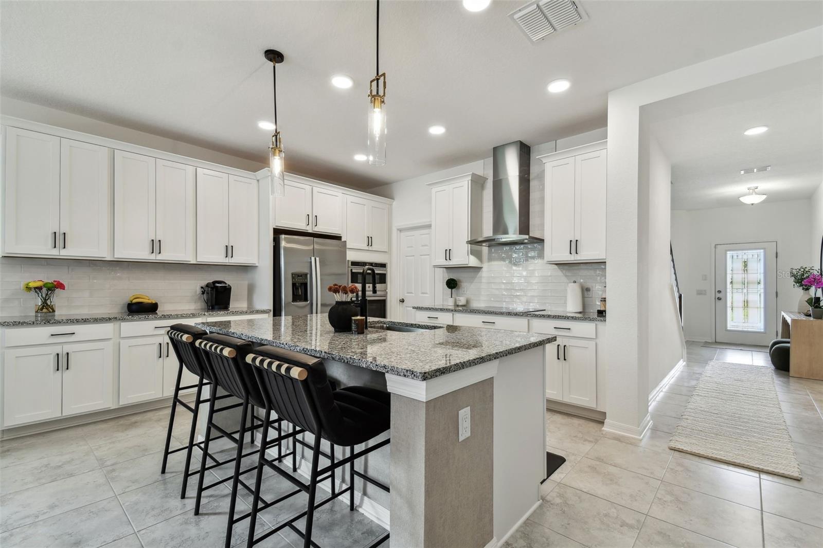 Custom backsplash tile. Additional pendant lights and designer wallpaper detail on island.