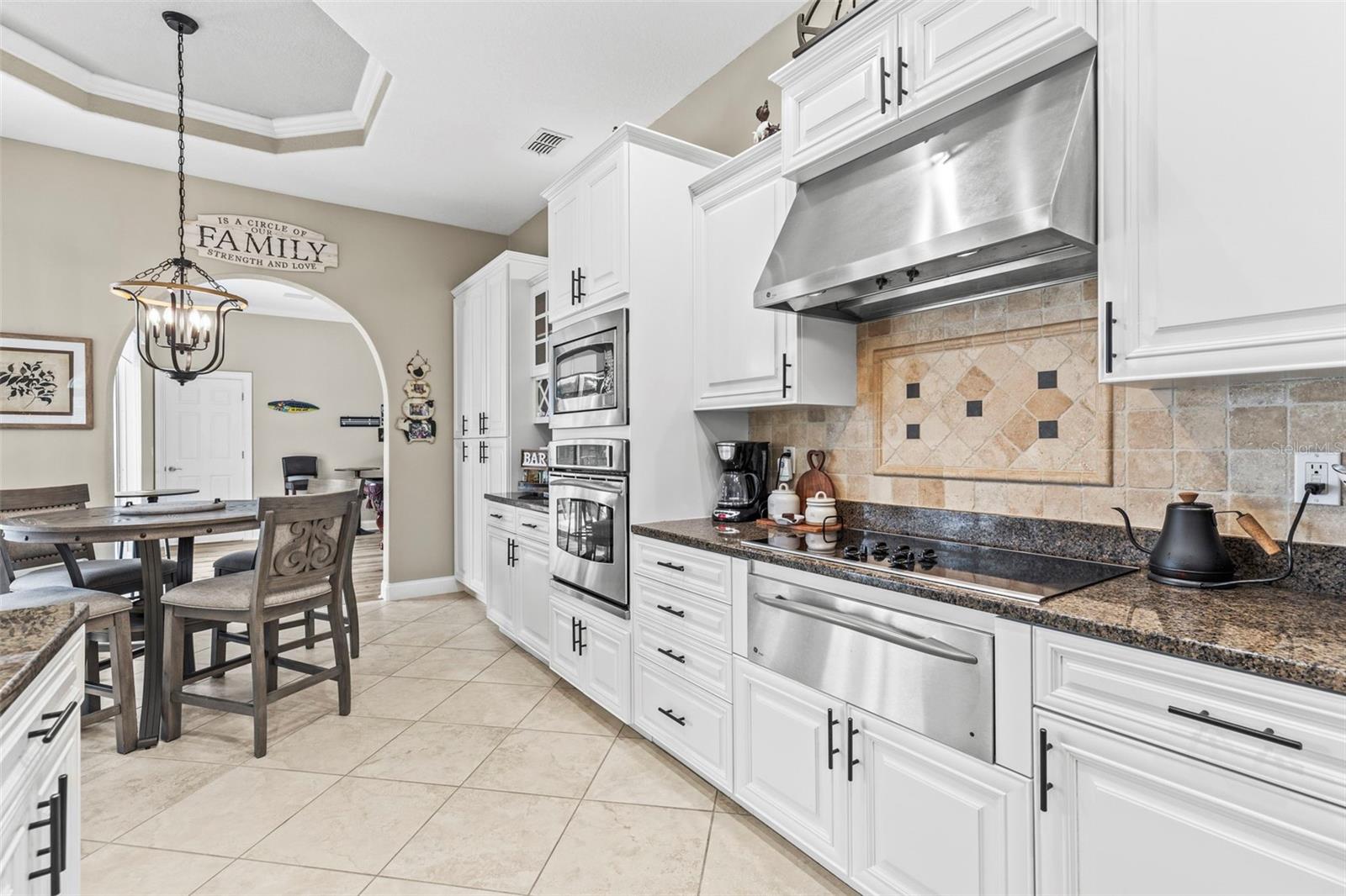 Five burner cooktop with patterned tile back splash and stainless steel hood