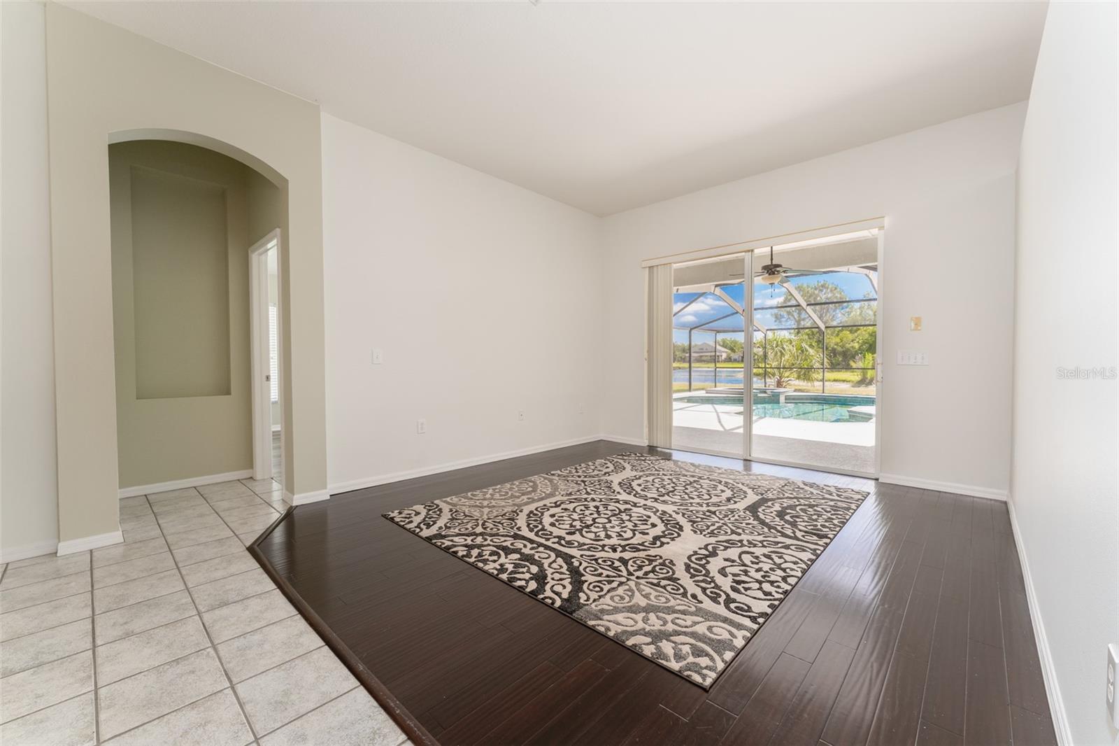 formal living room with a wood floor & sliding glass doors for a beautiful view of the pool & pond. Doorway to the primary suite is shown.