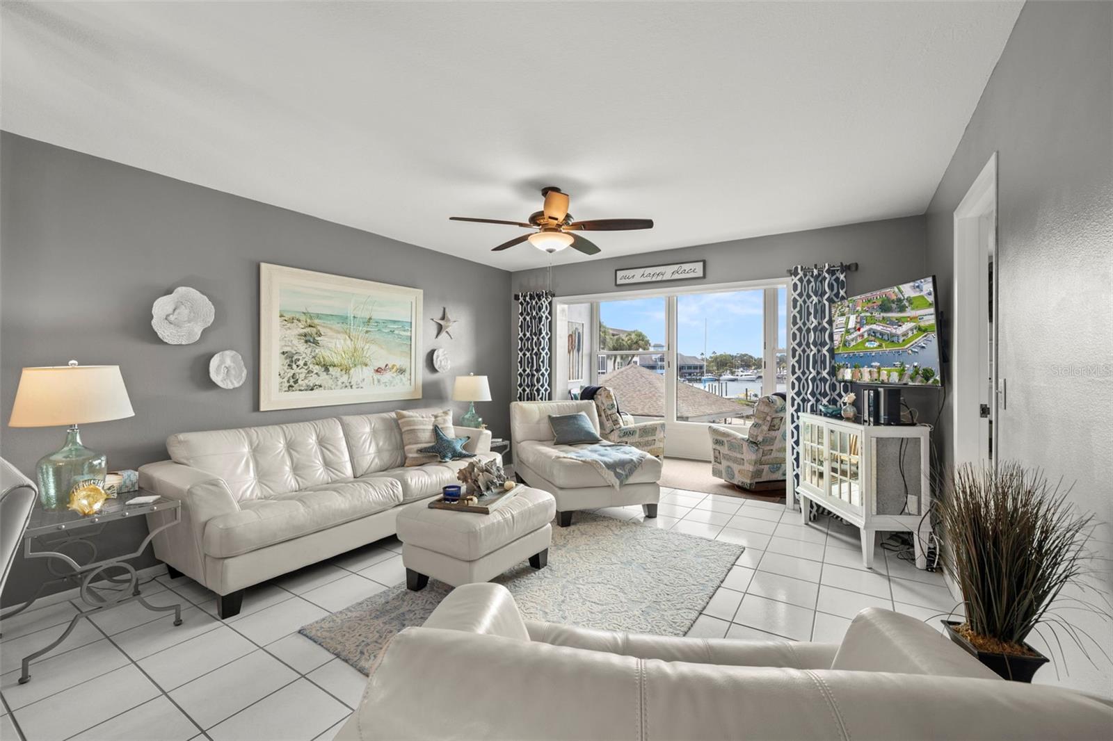 Charming coastal themed move-in ready condo that has all the views (canal, pool and city)! This is the main living area of the home with on-trend paint choices, scraped ceiling, ceiling fan, ceramic tile flooring AND an enclosed balcony with windows to the ceiling!