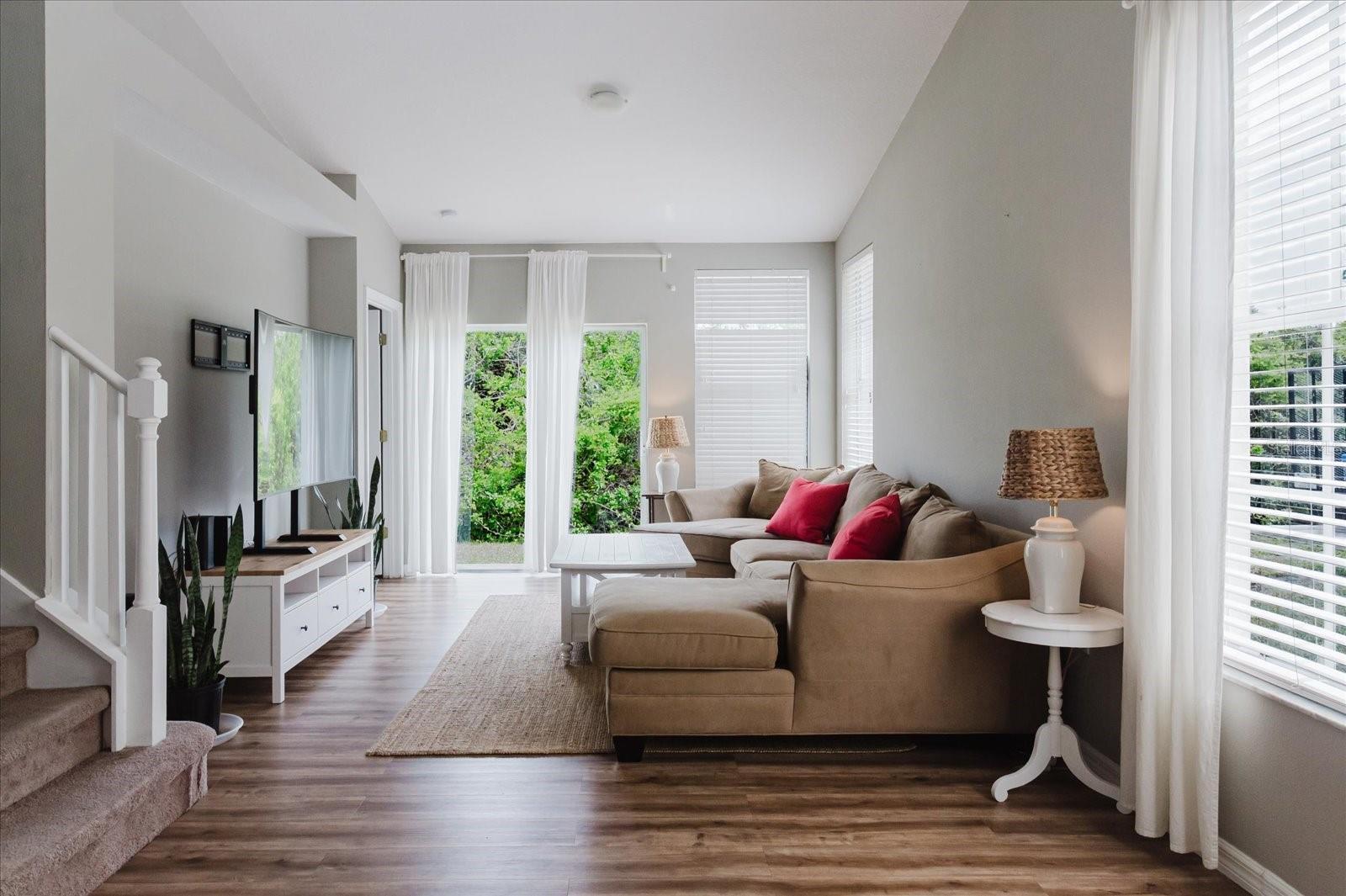 Open Concept Main Living Area With HIGH CEILINGS and Luxury Vinyl Floors, Sliding Glass Door Leads To Patio That Overlooks A Wood Area 1